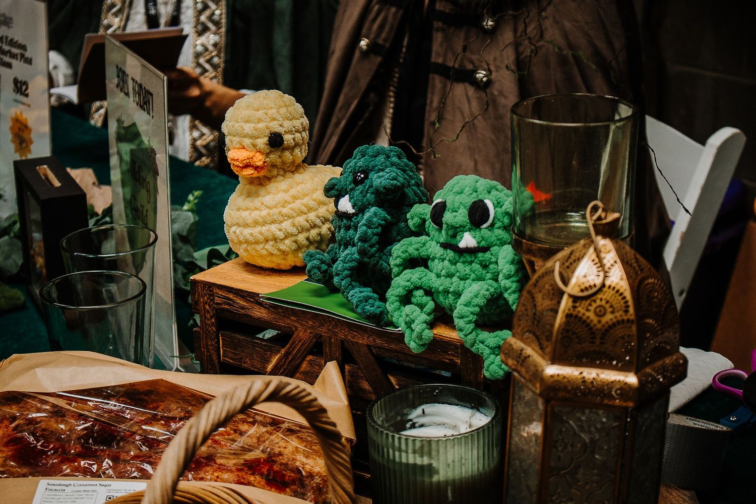 Handmade crochet amigurumi toys including a duck and monsters displayed at a fantasy market vendor table.