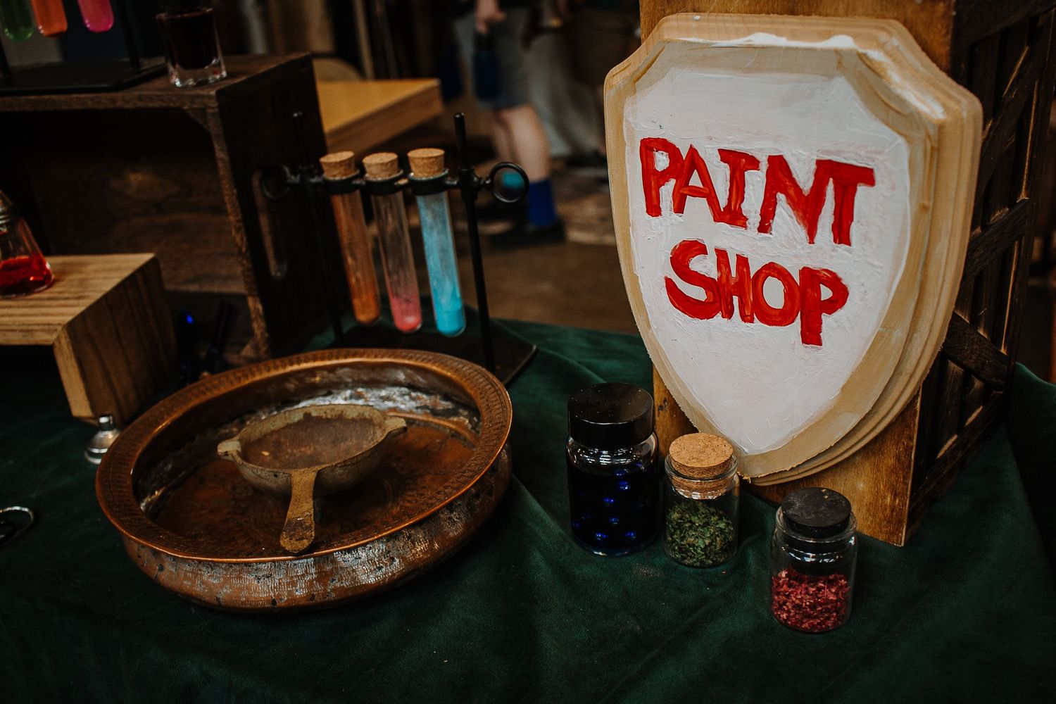 Fantasy themed Paint Shop display with colorful ink bottles and shield sign at a tabletop gaming market.
