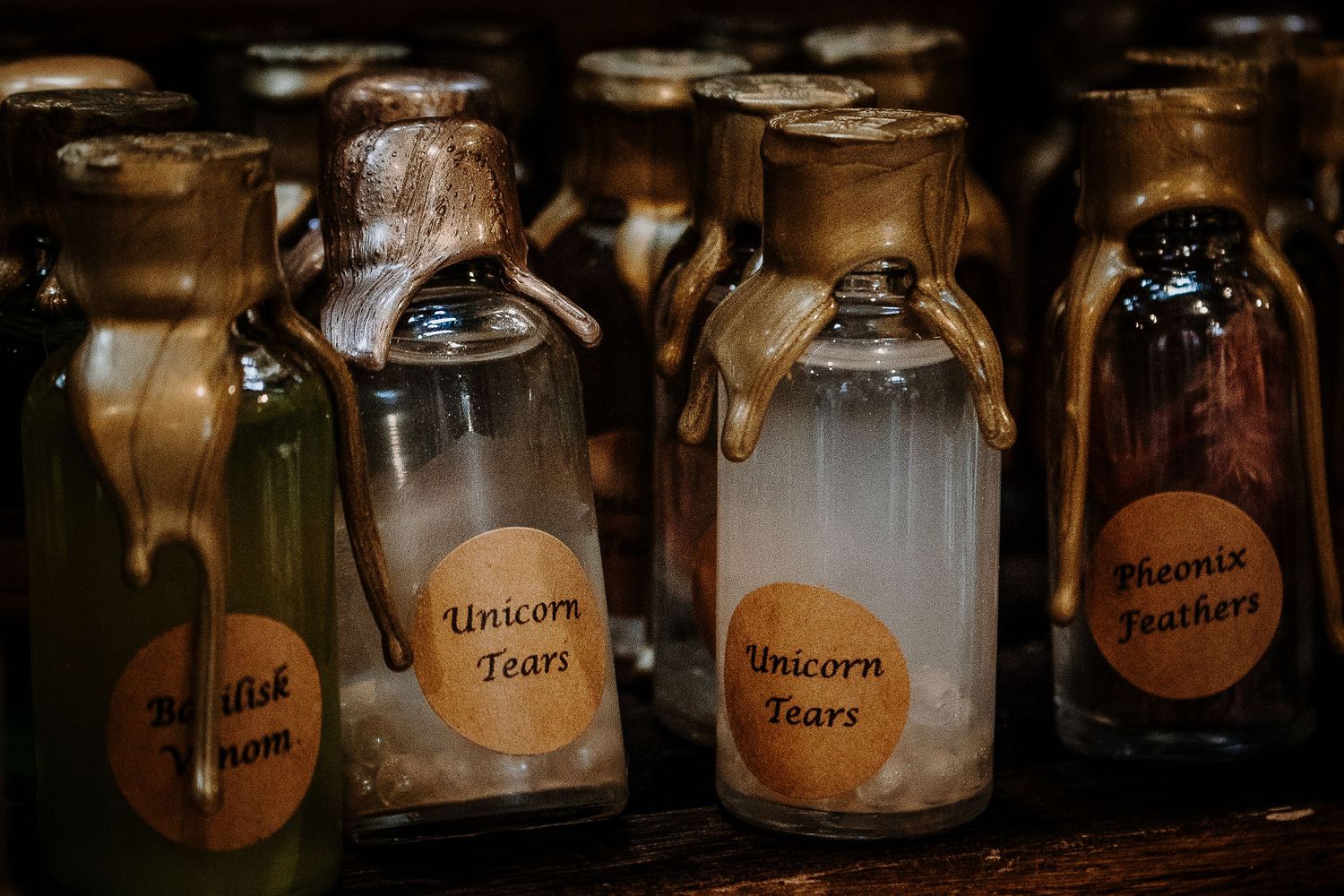 Decorative glass bottles labeled Unicorn Tears and Phoenix Feathers on a wooden shelf.