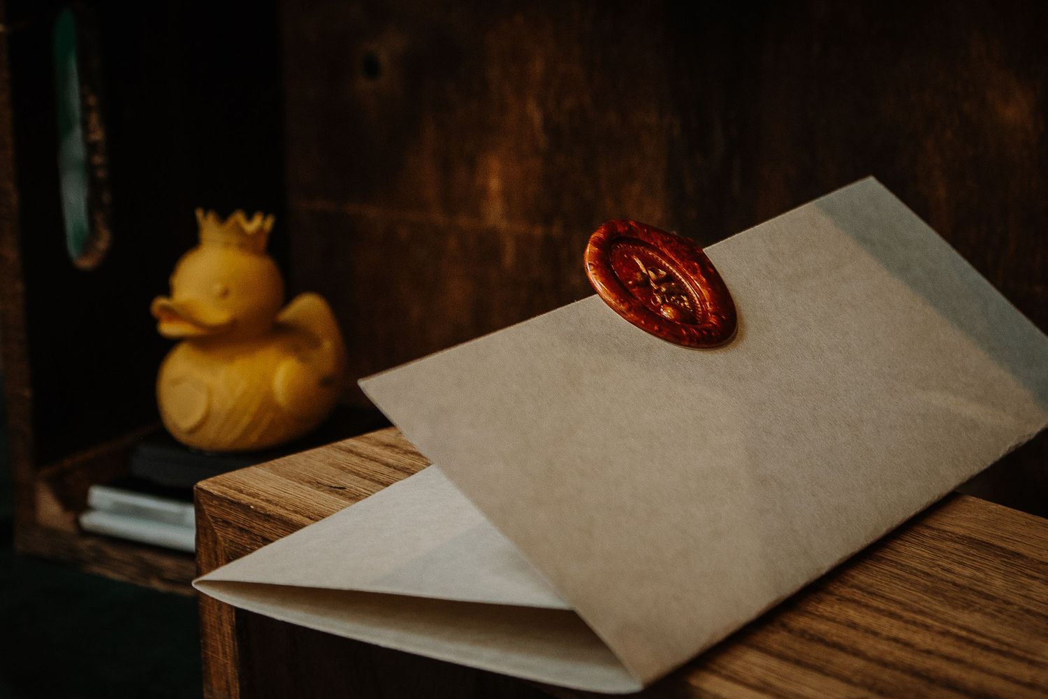 Kraft paper envelope sealed with red wax stamp beside a yellow rubber duck figurine on wooden surface.