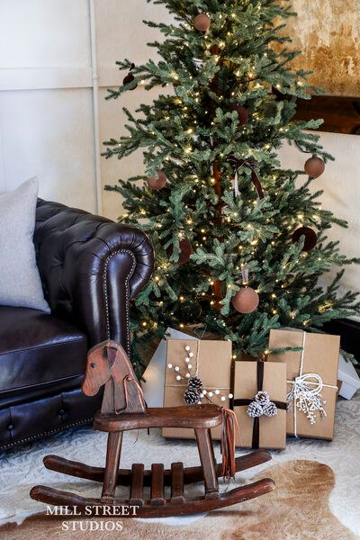 Cozy Christmas scene with lit tree, kraft paper gifts, pine cones, and a wooden rocking horse on a fur rug.
