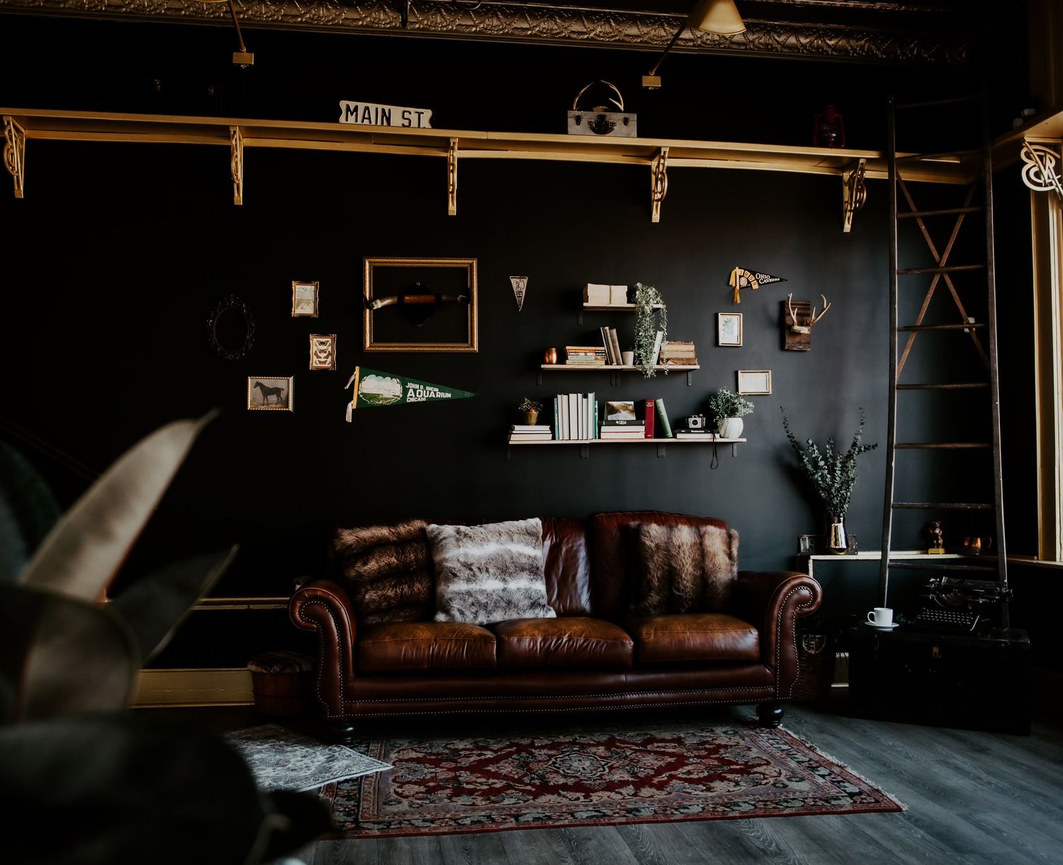 Dark moody living room with brown leather Chesterfield sofa, Persian rug, and gallery wall decor.