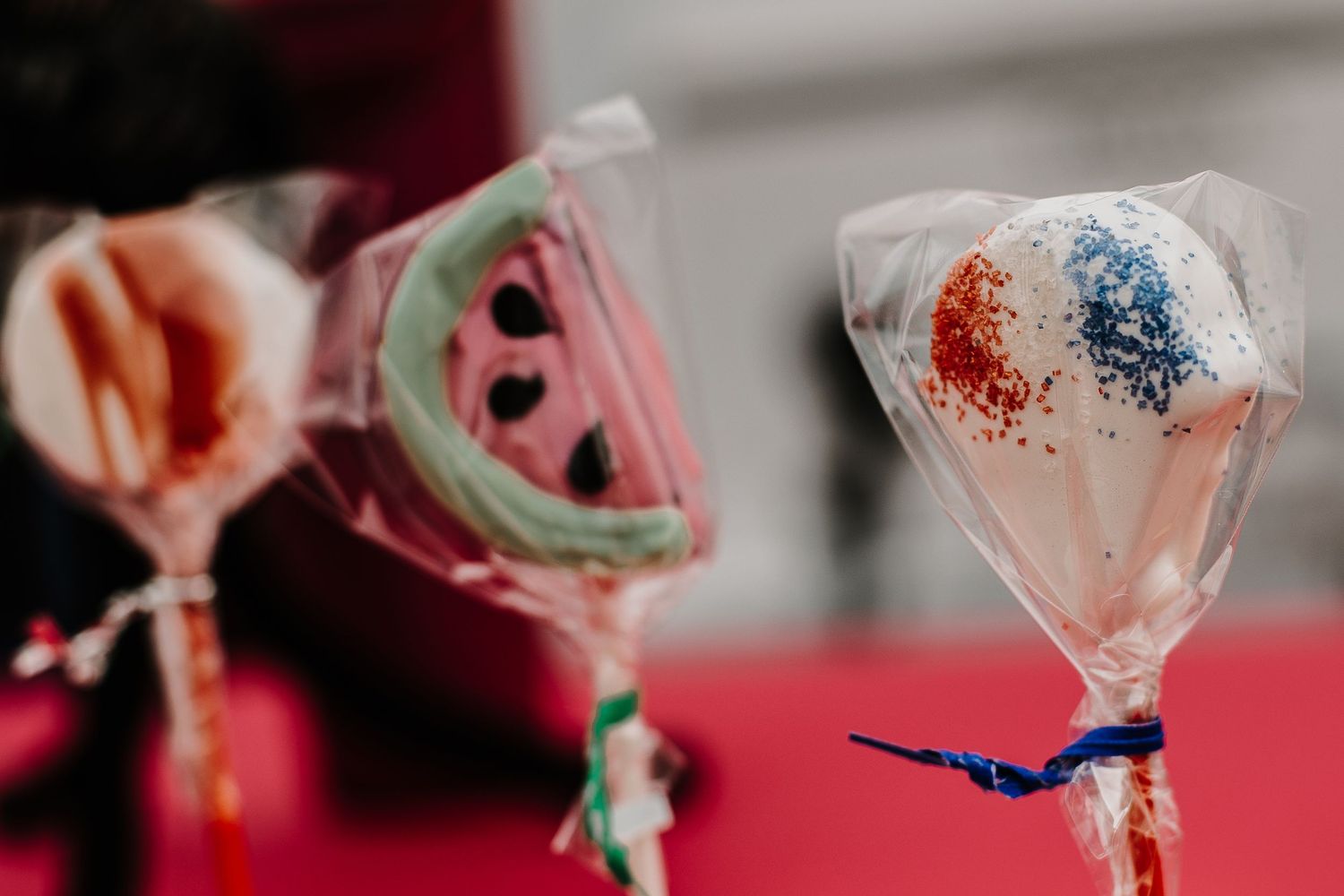 Red white and blue sprinkled cake pop and watermelon lollipop wrapped in clear cellophane.
