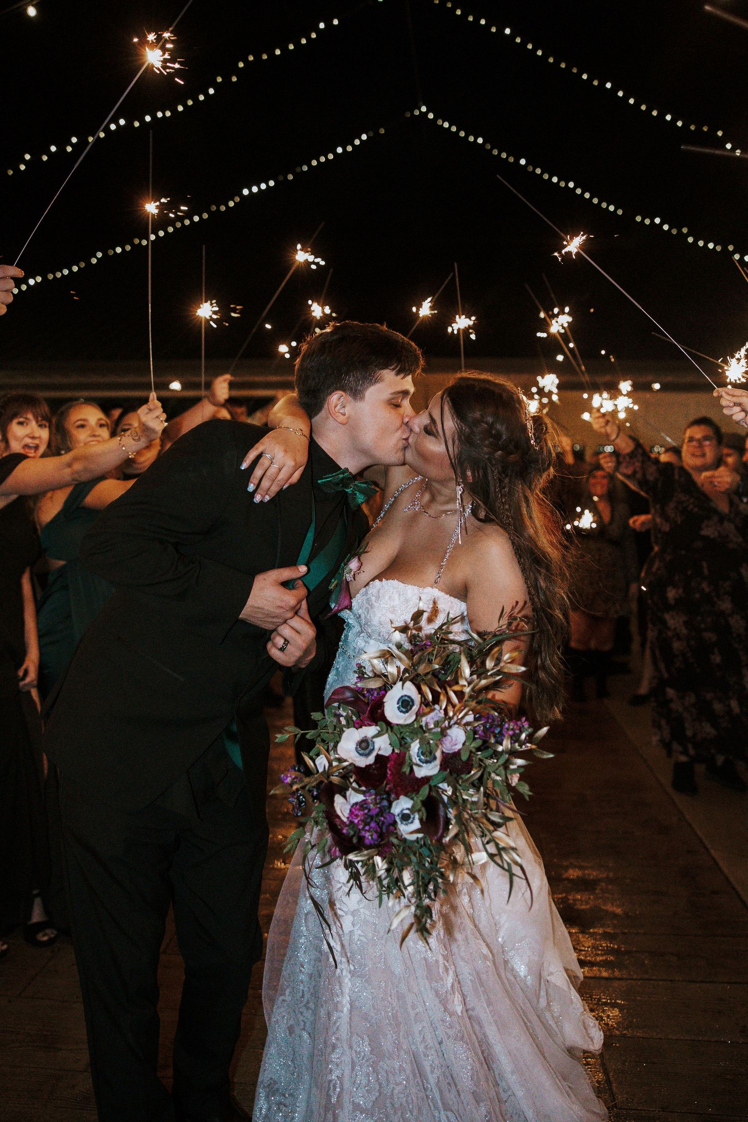Bride and groom share a kiss during a sparkler send-off at their outdoor wedding reception at night.