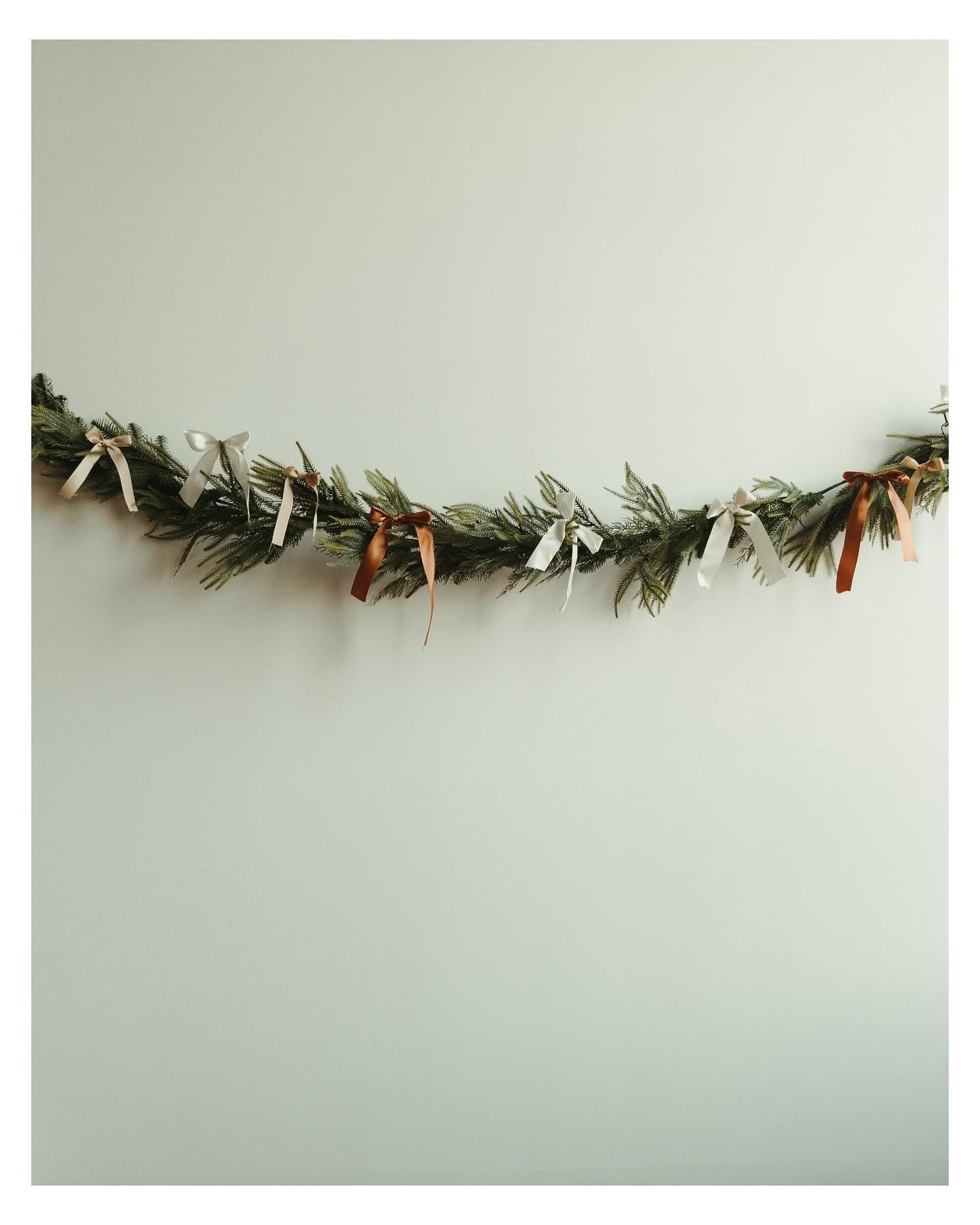 A festive evergreen garland adorned with colorful ribbons hung against a light green wall.