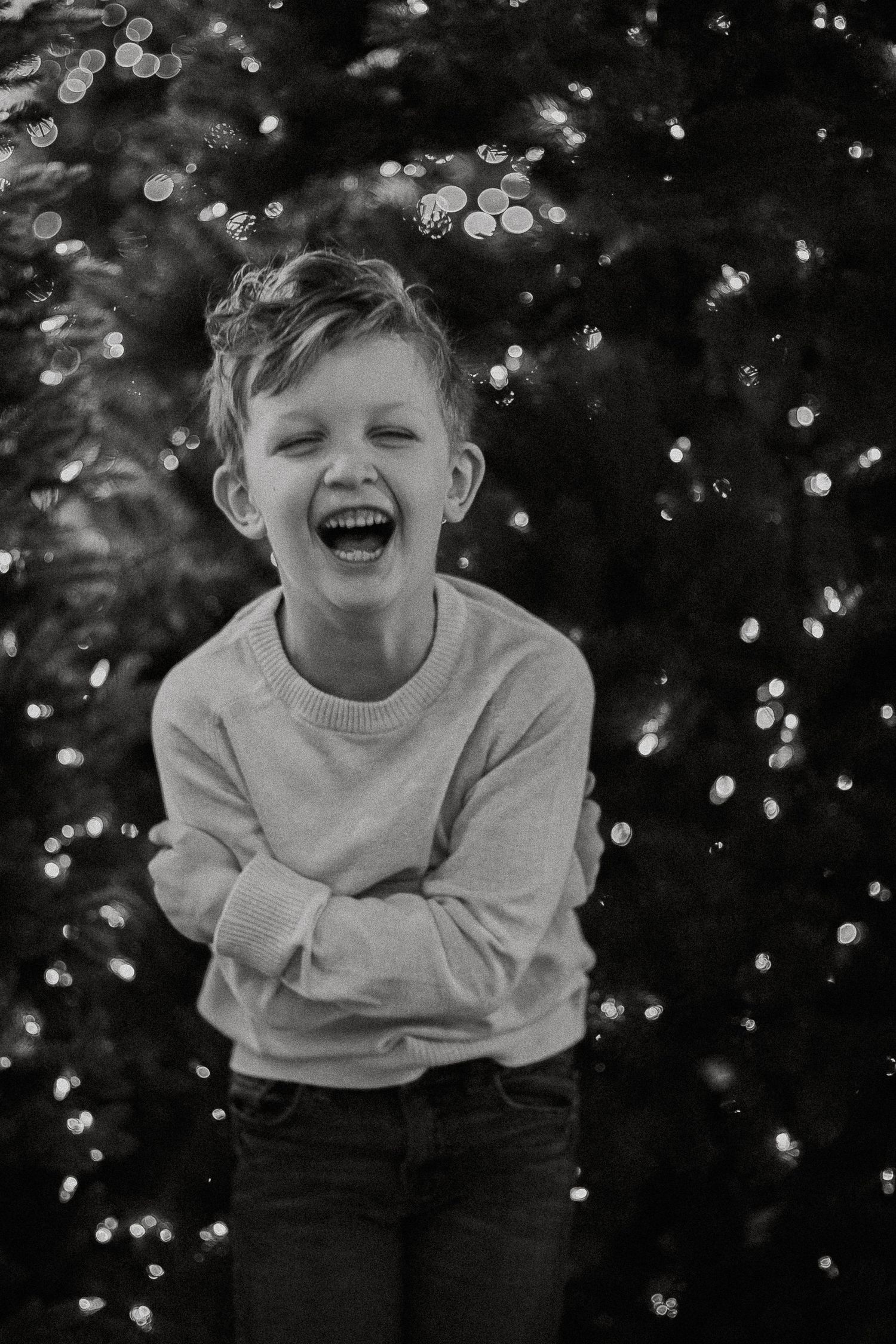 Black and white photo of a laughing boy in a sweater with bokeh lights in the background.