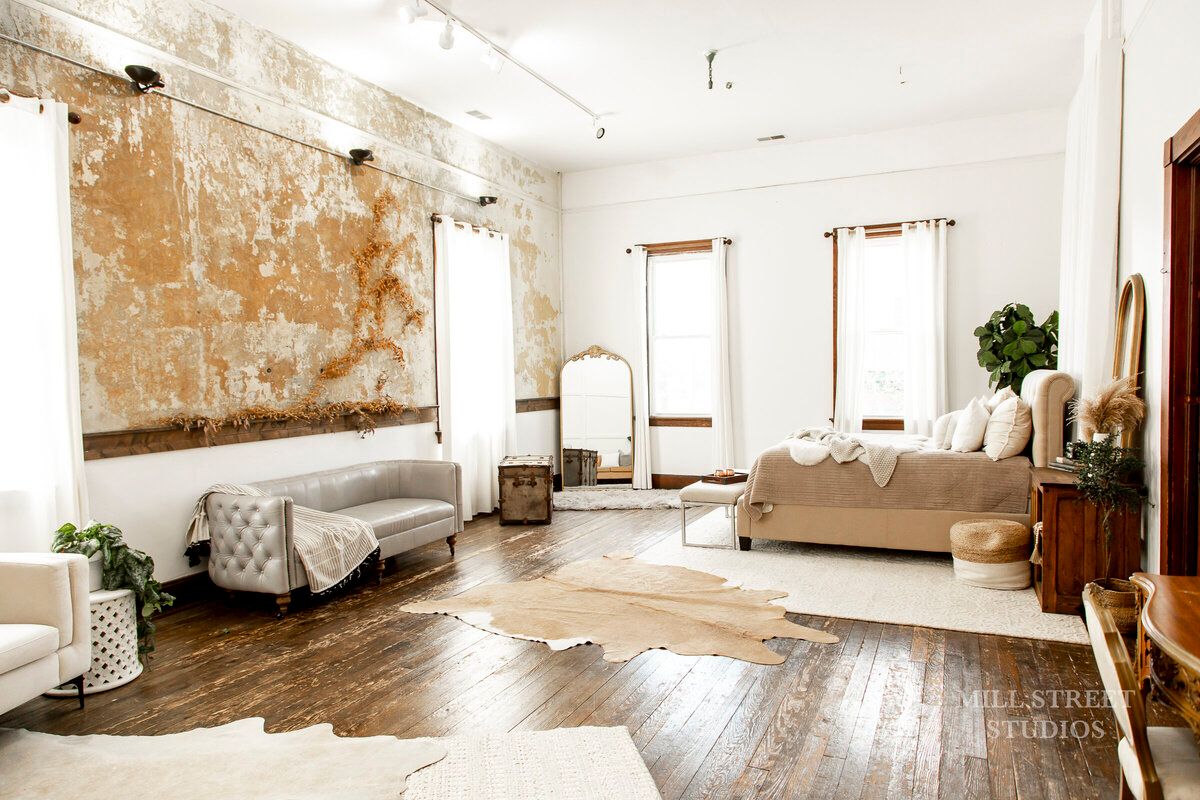 Rustic boho studio with distressed accent wall, linen bed, cowhide rug, and neutral furnishings.
