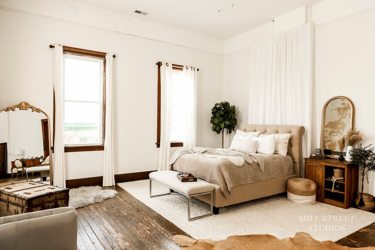 Bright boho bedroom with linen bed, cowhide rug, vintage mirror, wood floors, and neutral decor.