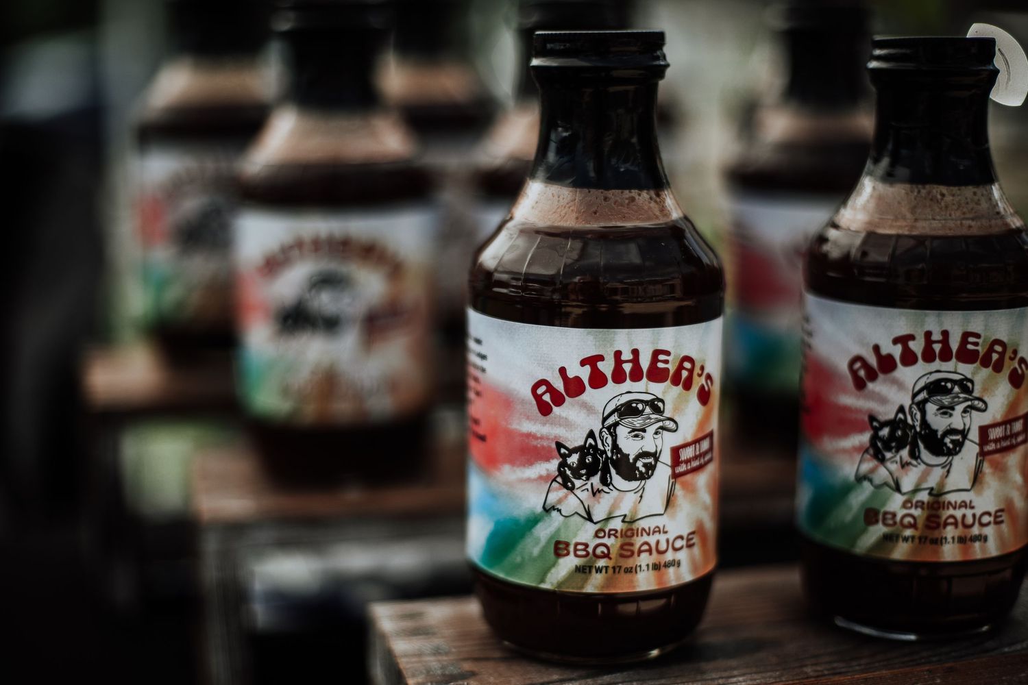 Multiple bottles of Althea's BBQ Sauce displayed on a wooden surface at an outdoor market.