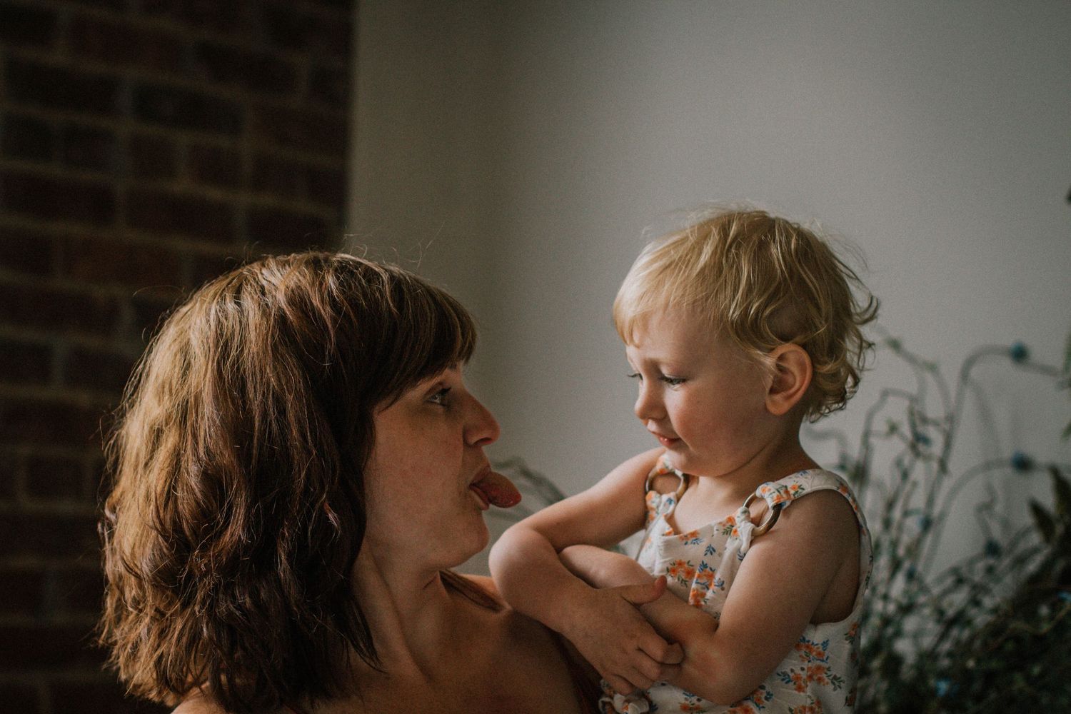 Mother tenderly holding and gazing at blonde toddler daughter in soft natural light.