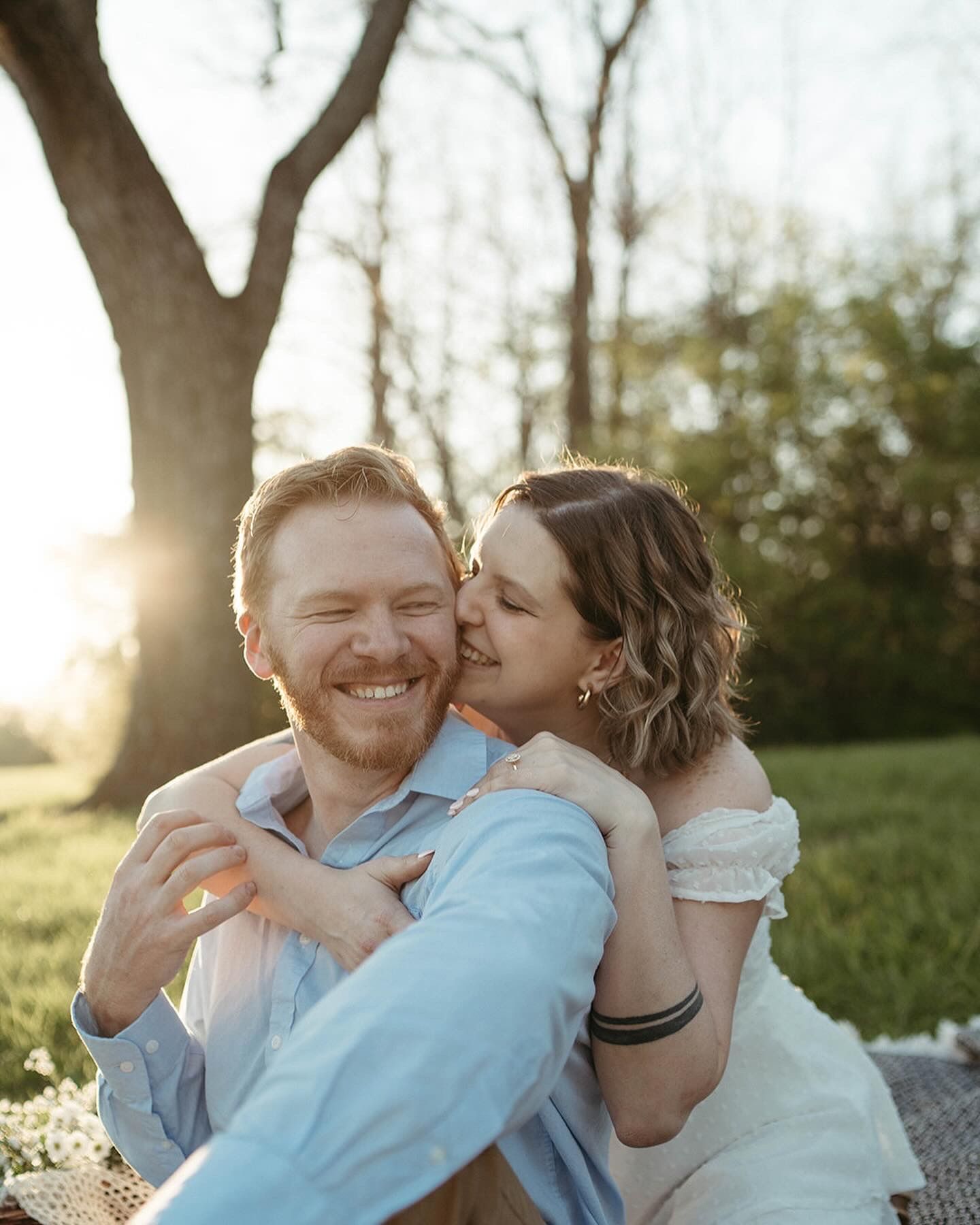 Couple sharing a romantic moment at golden hour outdoors, woman kissing mans cheek while he smiles joyfully.