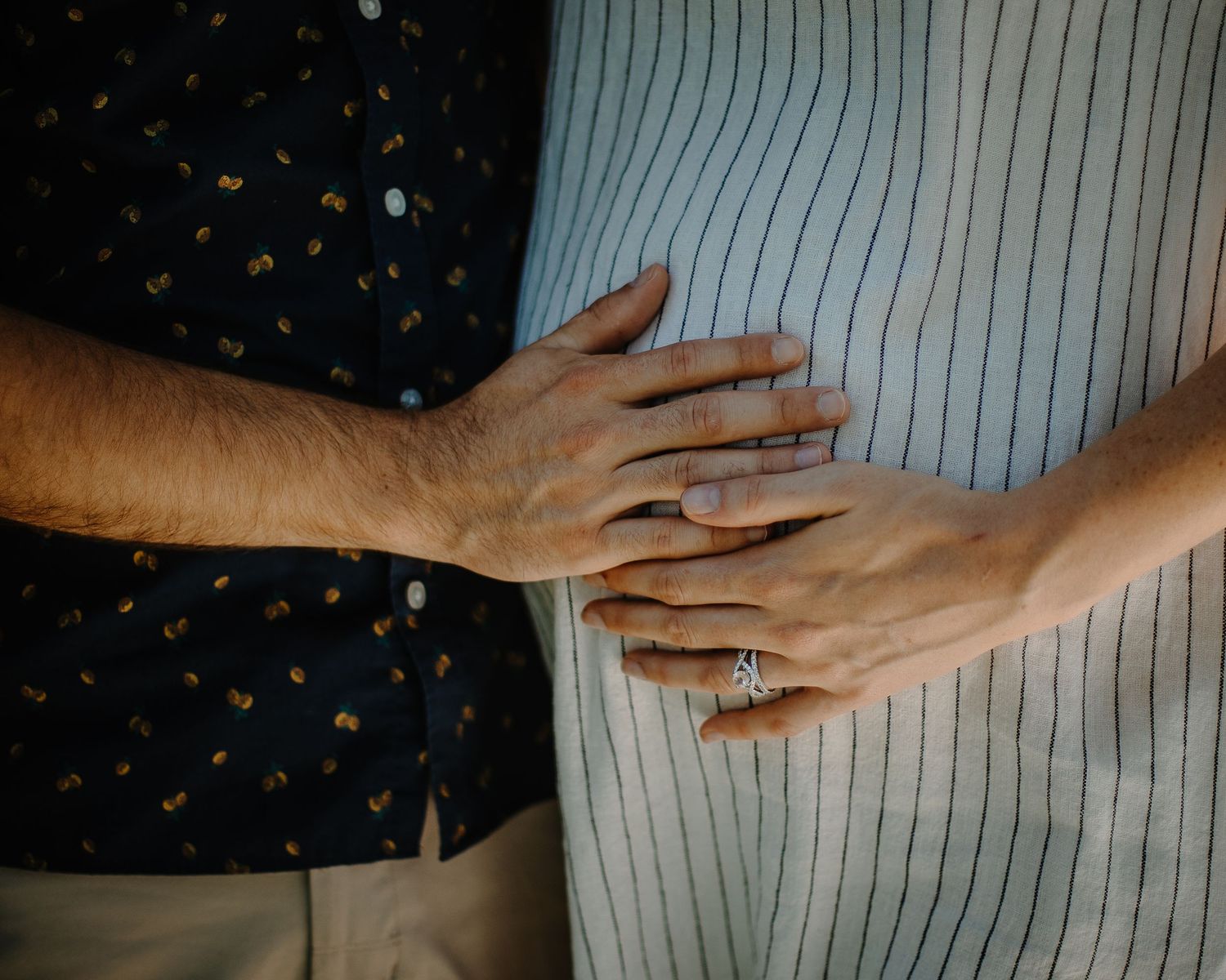 Close-up of a couple holding hands, woman wearing a diamond engagement ring, standing together.