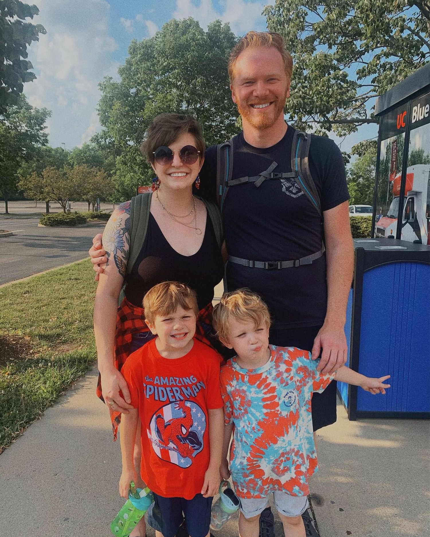 Happy family of four posing outdoors on sunny day near bus.