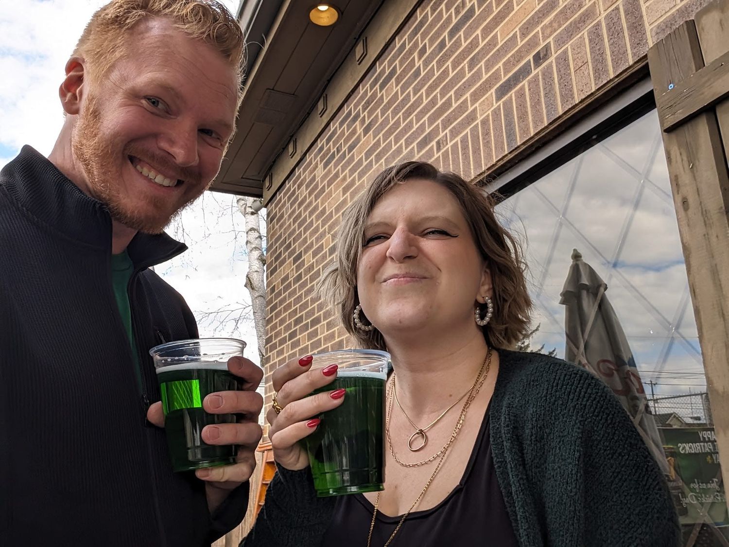 Couple smiling and toasting with green drinks outdoors on St. Patricks Day.