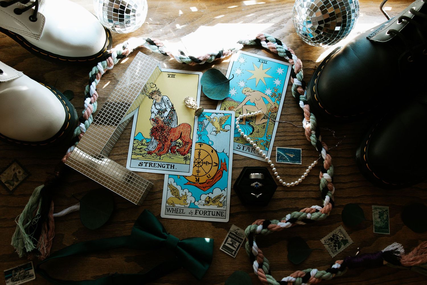 Tarot cards including Strength and Wheel of Fortune spread on wooden table with boots, bow tie, pearls, and disco ball.