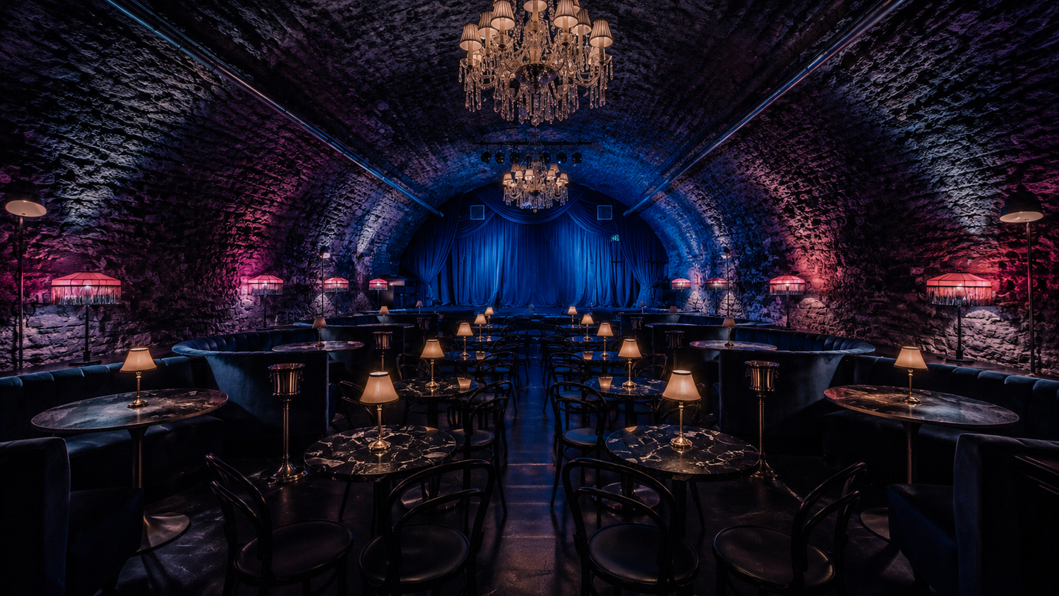 Elegant underground vaulted dining room with dark stone arches, chandelier, candlelit tables, and dramatic blue and purple lighting.