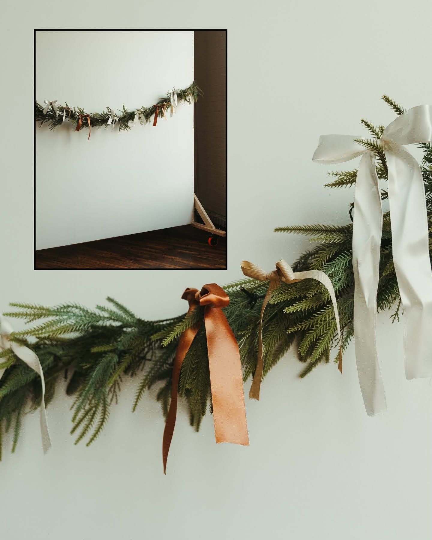 Festive evergreen garland with satin ribbons in white, rust, and cream draped on a white wall for holiday decor.