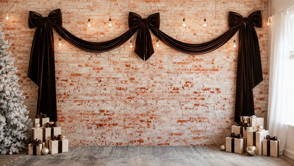 Festive brick wall backdrop with black bow drapes, hanging Edison bulbs, wrapped gifts, and a white Christmas tree.