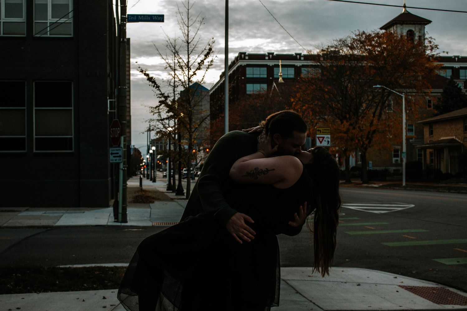 Couple sharing a romantic dip kiss on an urban street corner during autumn twilight.
