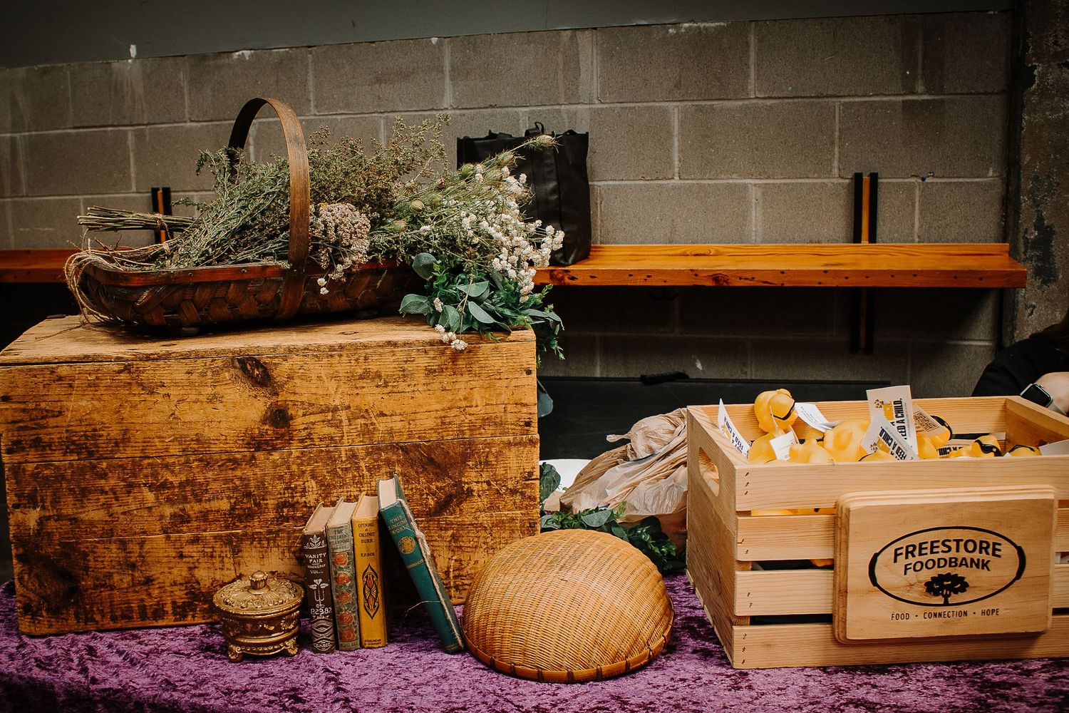 Rustic wooden crates with dried flowers, books, and vintage items displayed on a purple cloth table.