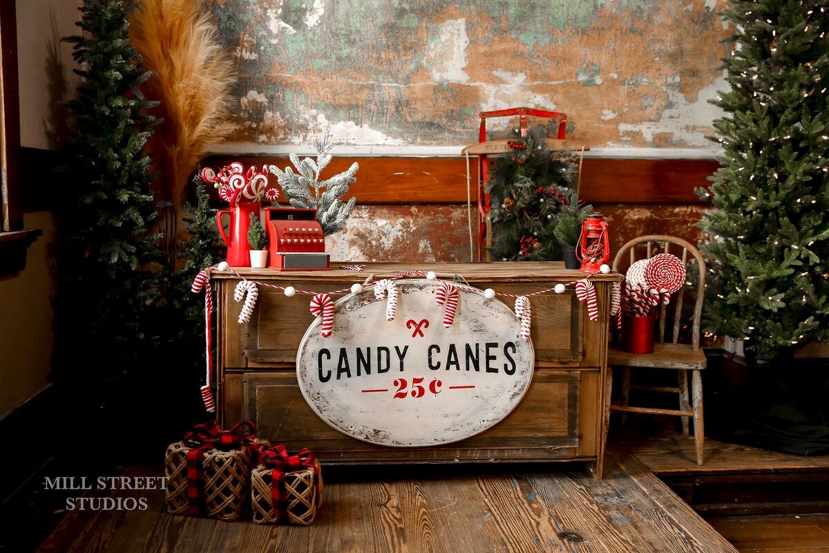 Festive Christmas backdrop with candy canes sign, decorated trees, and wrapped gifts by Mill Street Studios.