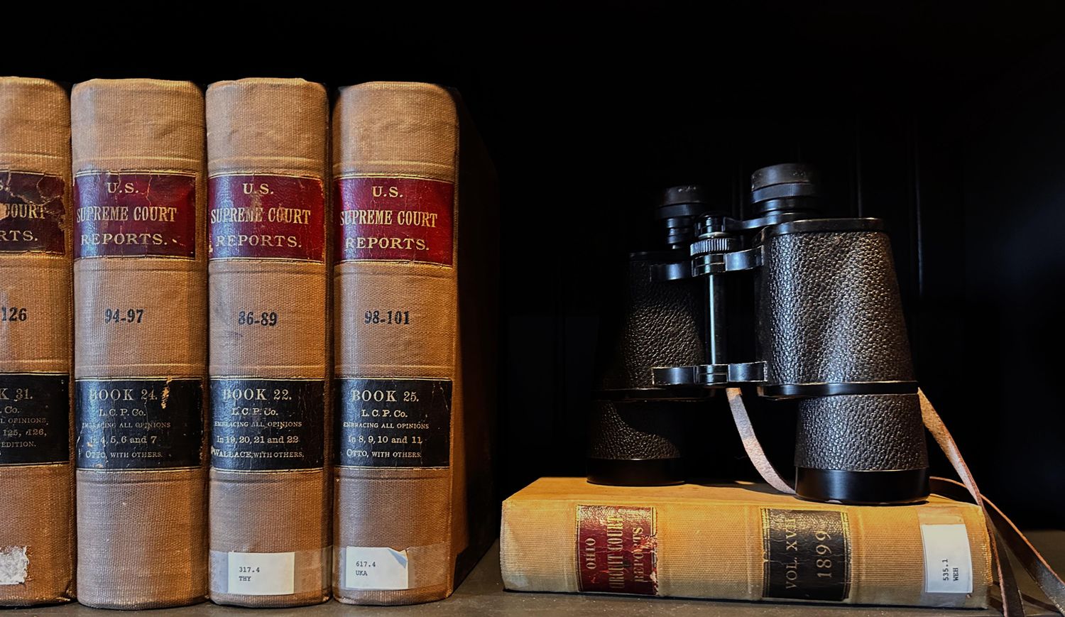 Vintage U.S. Supreme Court Reports law books on a shelf with classic binoculars resting on top.