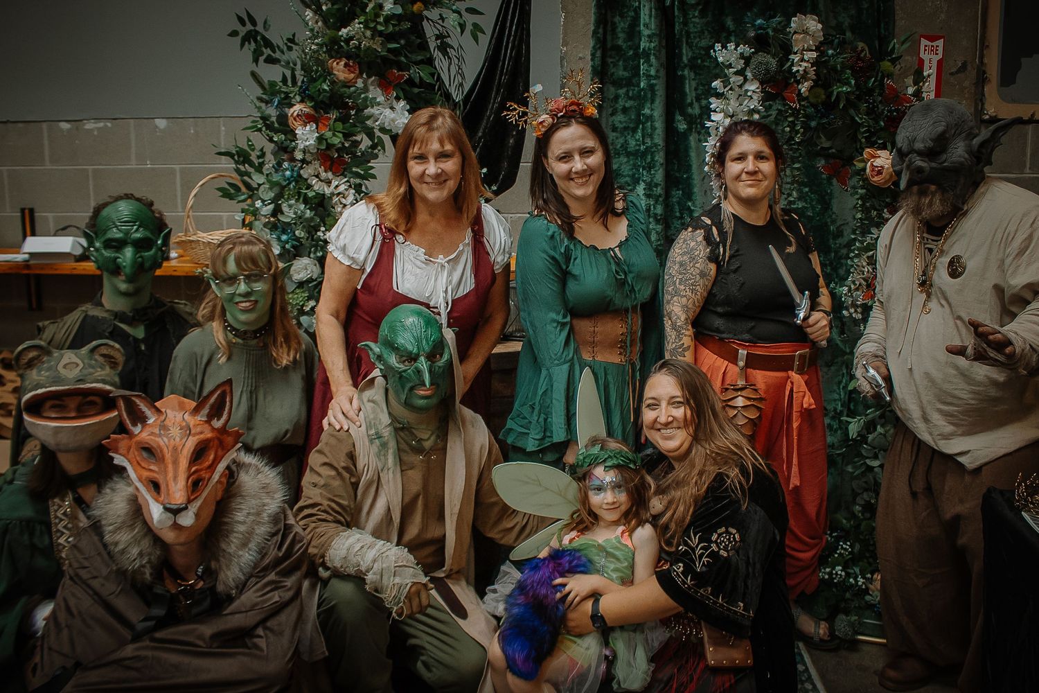 Group of fantasy cosplayers in elaborate creature and medieval costumes pose together at a convention.