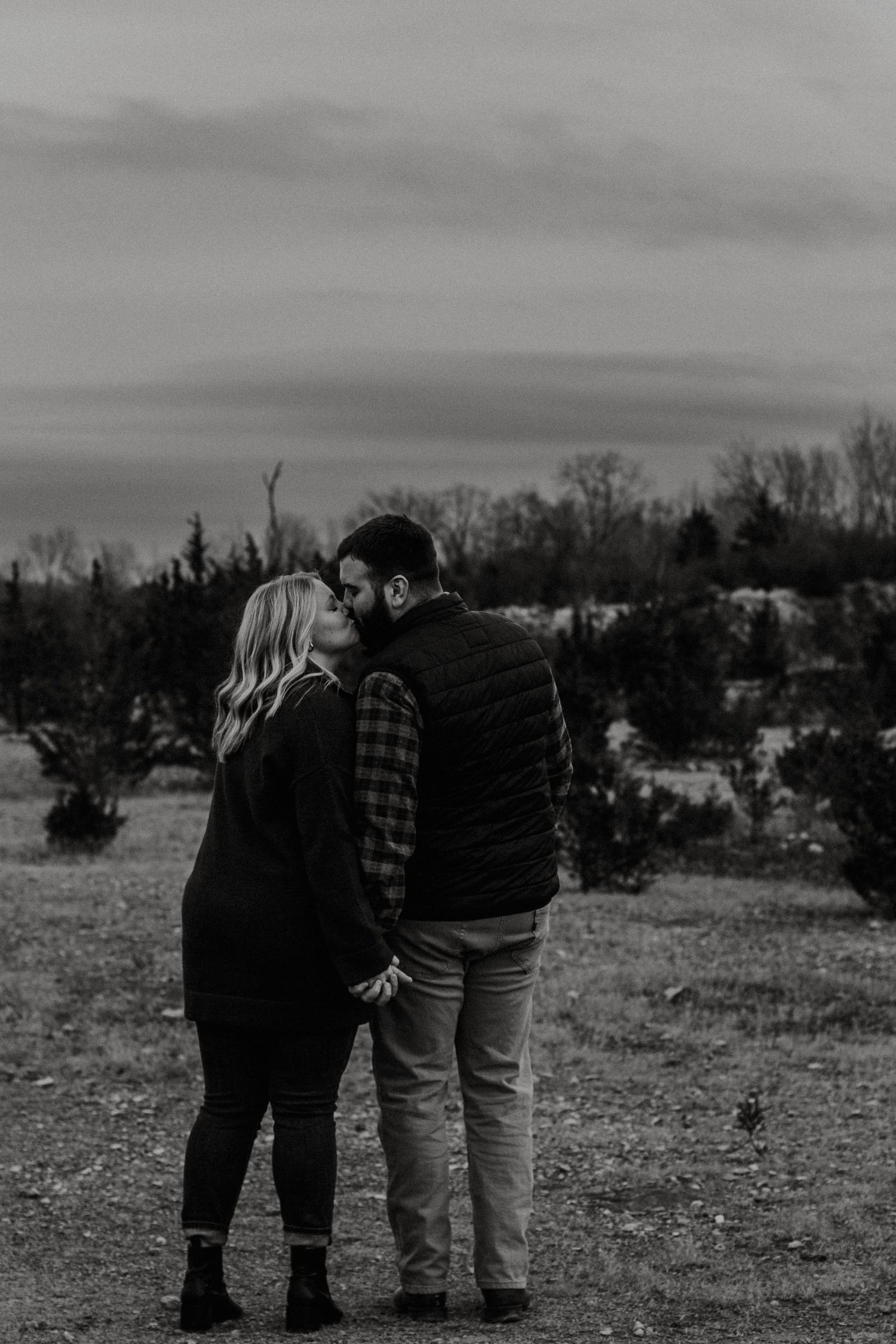 Black and white photo of couple holding hands in open field at dusk.