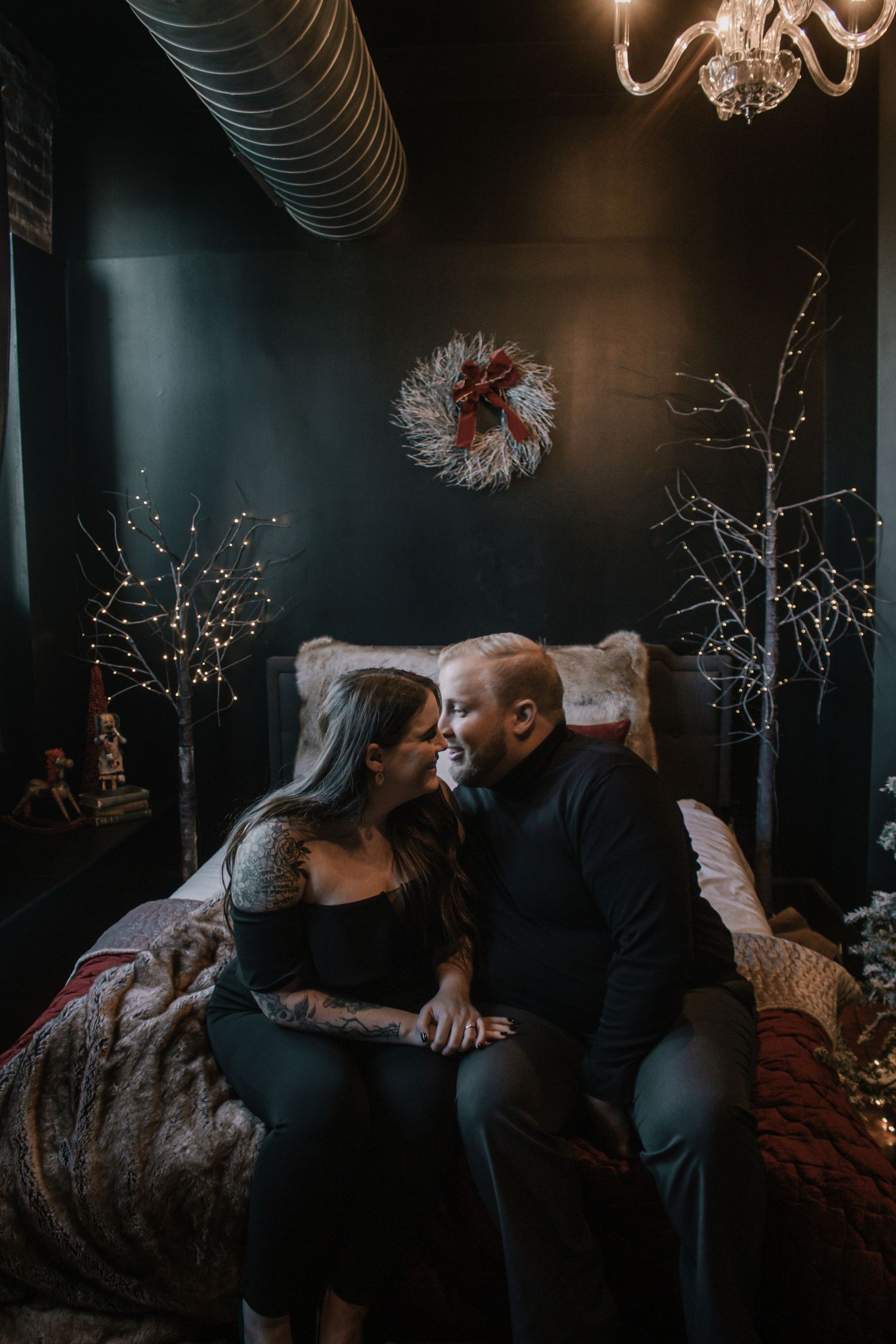 Romantic couple shares intimate moment on bed in dark room with Christmas wreath decor.