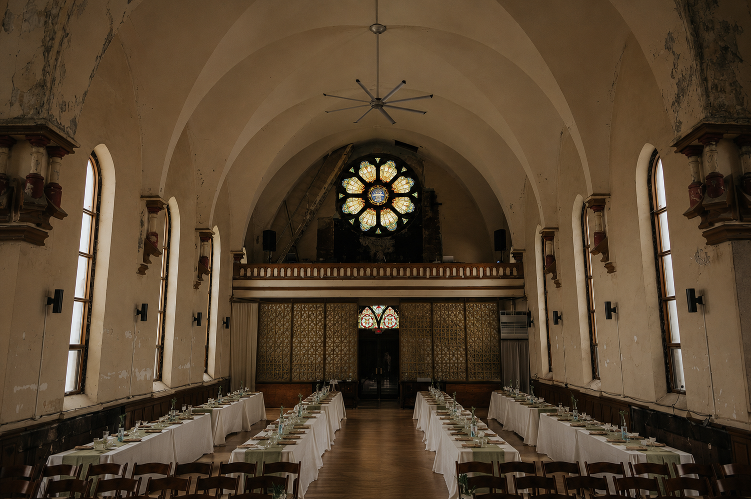 Elegant wedding reception hall with vaulted ceilings, stained glass rose window, and long decorated dining tables.