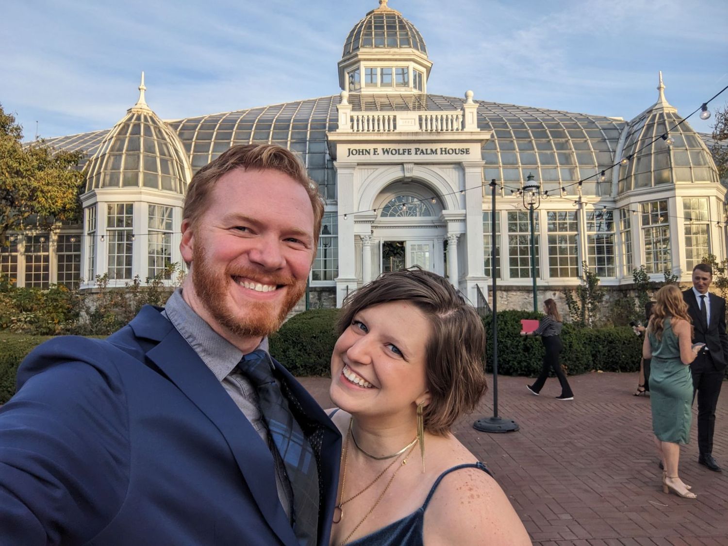 Smiling couple taking a selfie in front of the John S. Wolfe Palm House conservatory building.