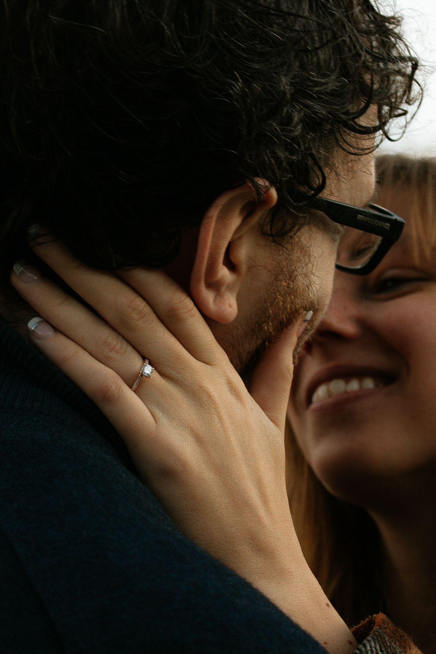 Close-up of a smiling woman with an engagement ring tenderly holding a mans face.