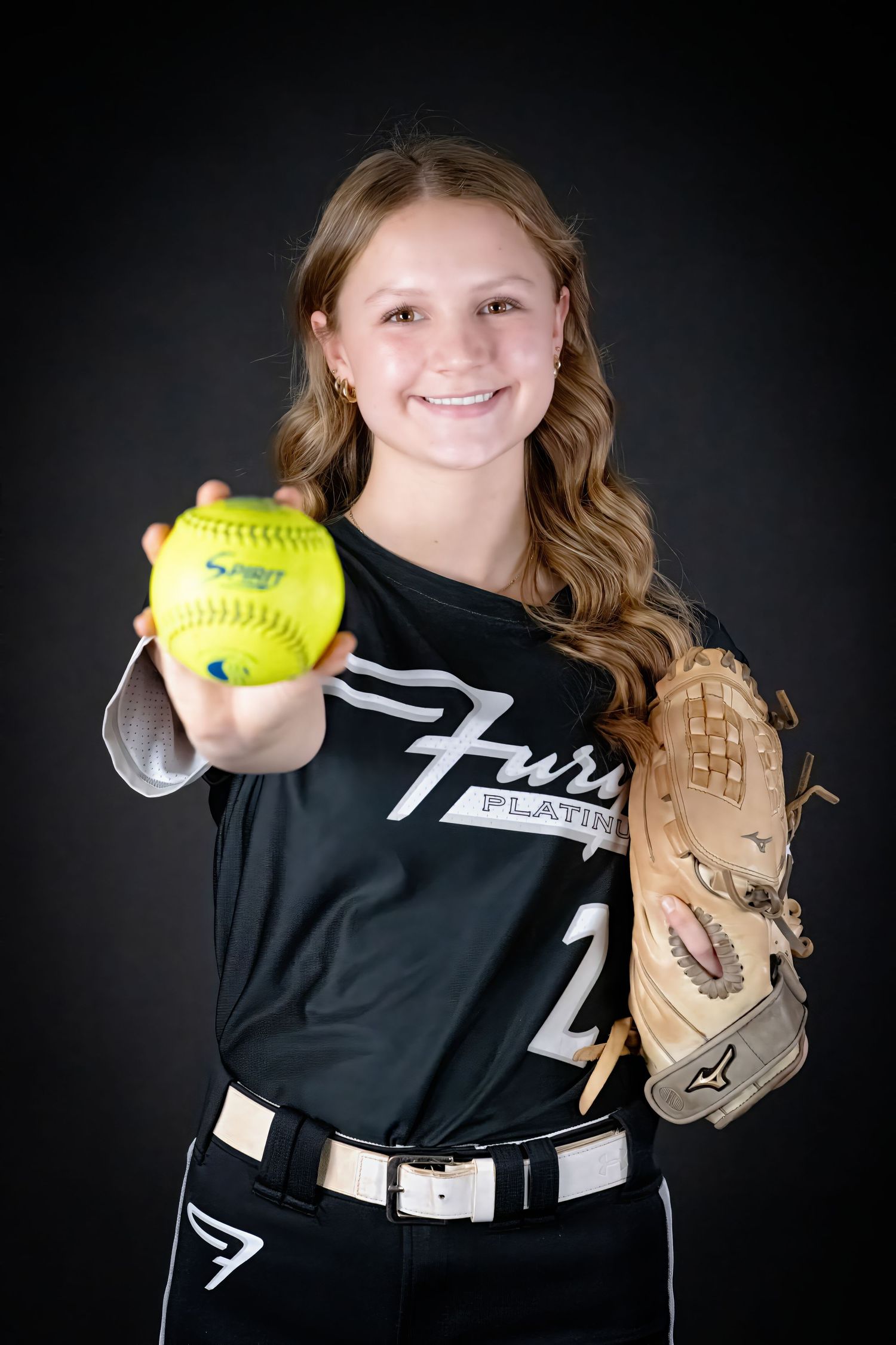 Young softball player in Fury Platinum black jersey holding yellow softball and glove.
