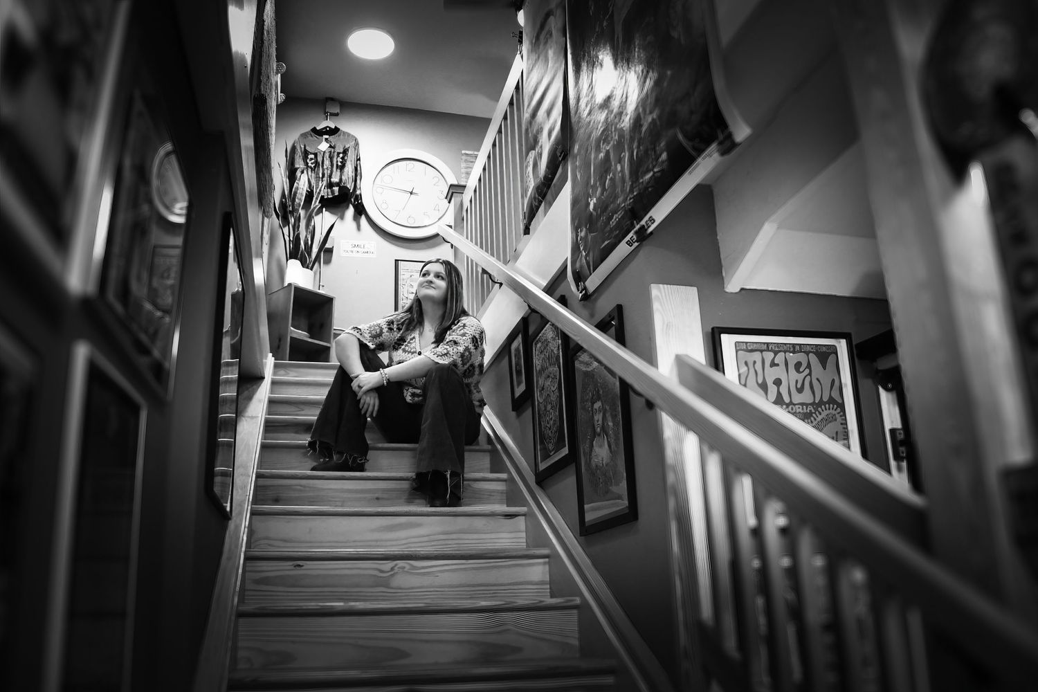 Black and white photo of person sitting on wooden staircase indoors.