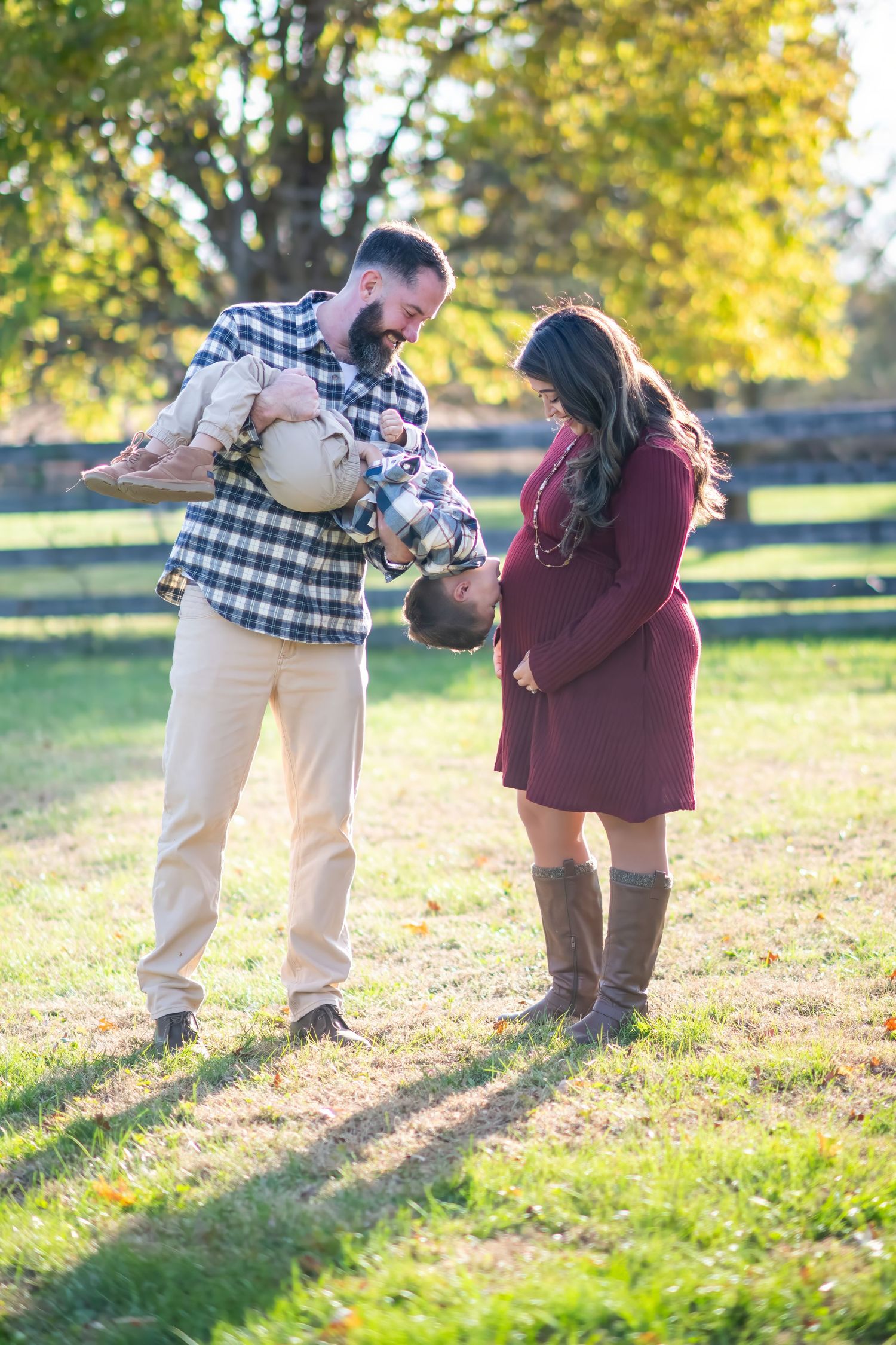 Expecting parents with young child holding pumpkin in sunny autumn field for maternity photo.