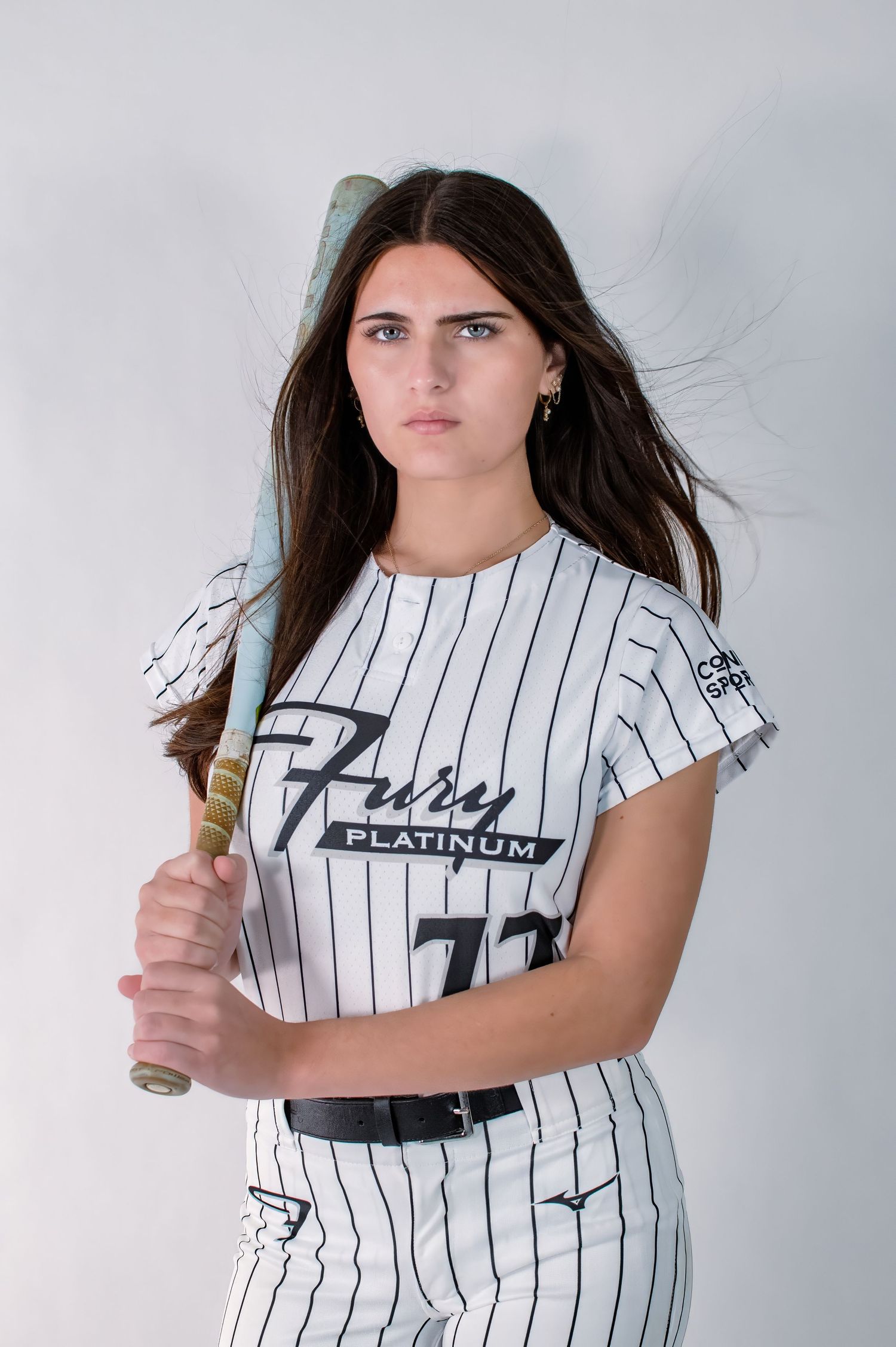 Female softball player #77 in Fury Platinum pinstripe jersey holding bat with intense look.