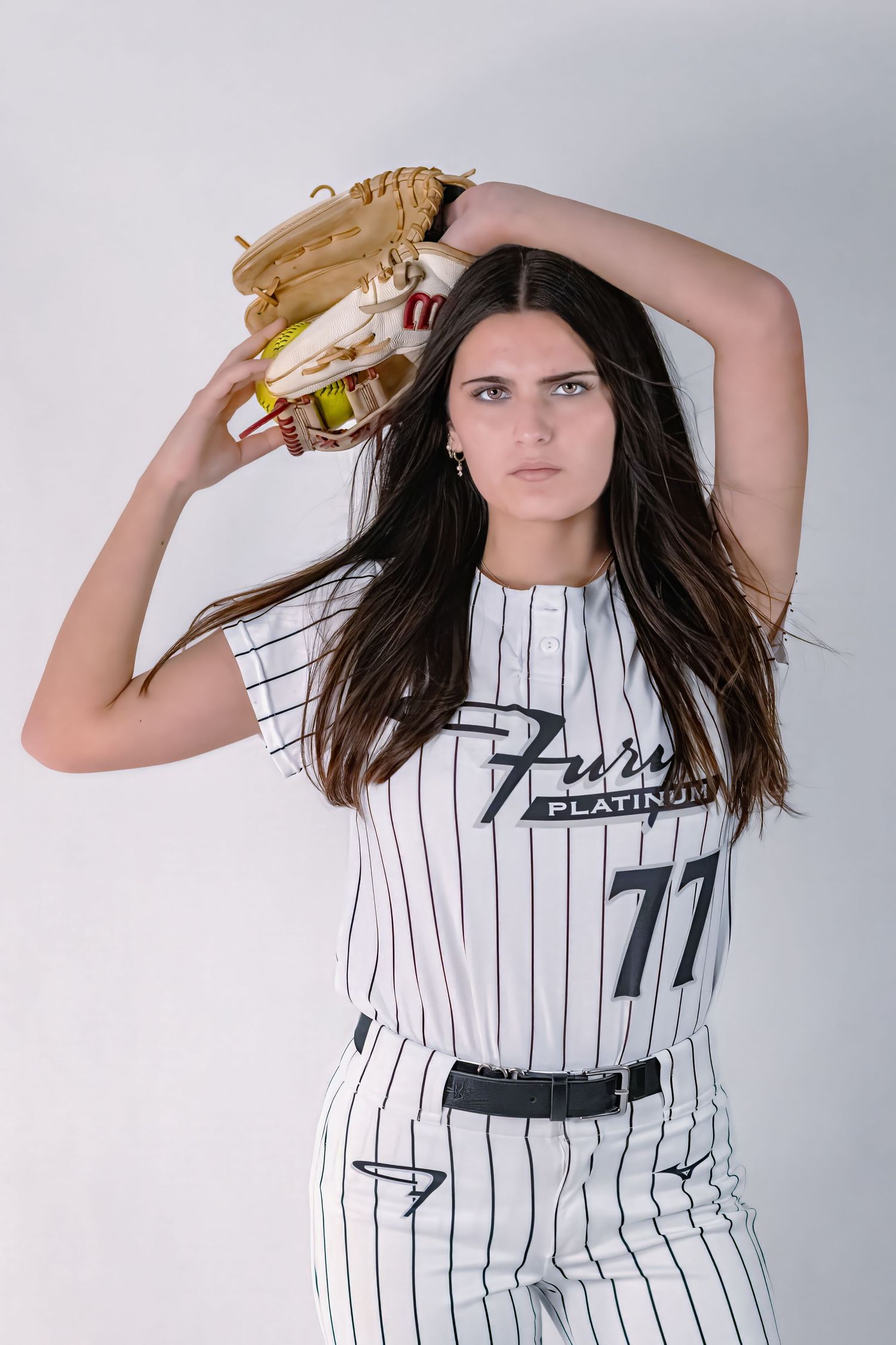 Softball player #77 in Fury Platinum pinstripe jersey posing with glove raised overhead.