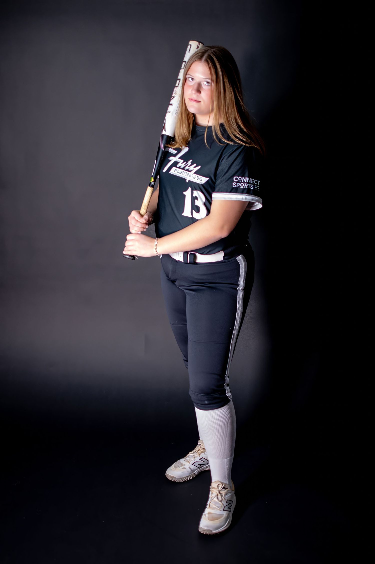 Female softball player in black Fury number 13 jersey holding bat in studio.