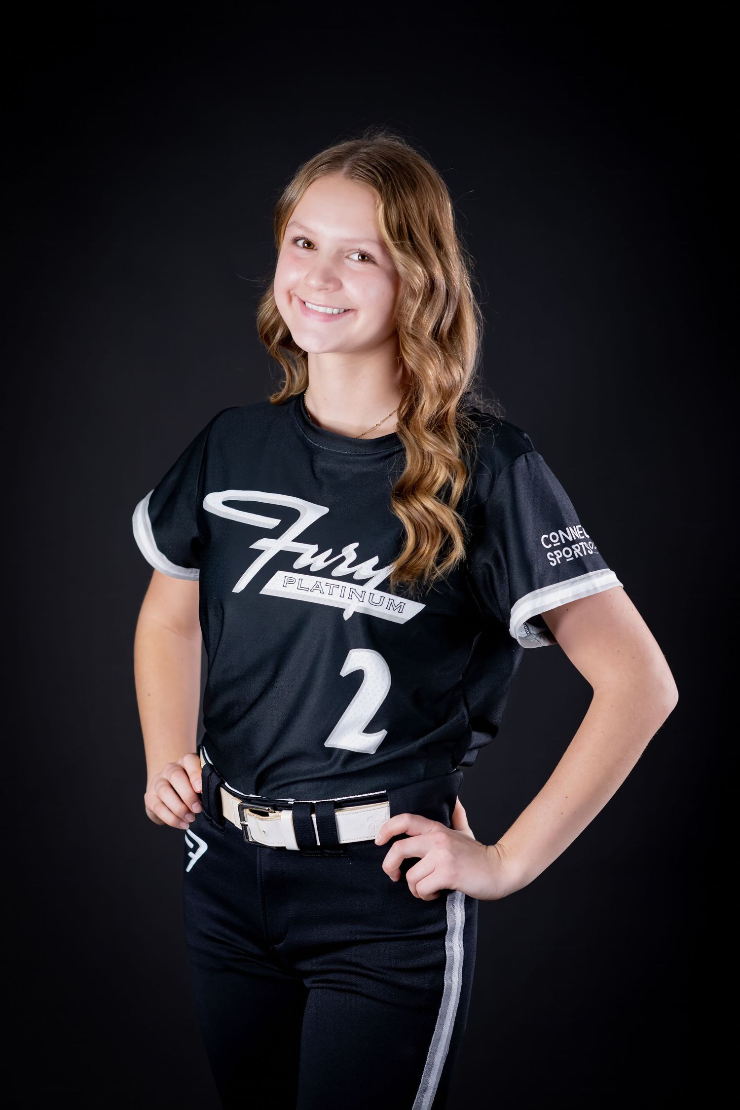 Young softball player in black Fury Platinum number 2 jersey posing with hands on hips in studio.