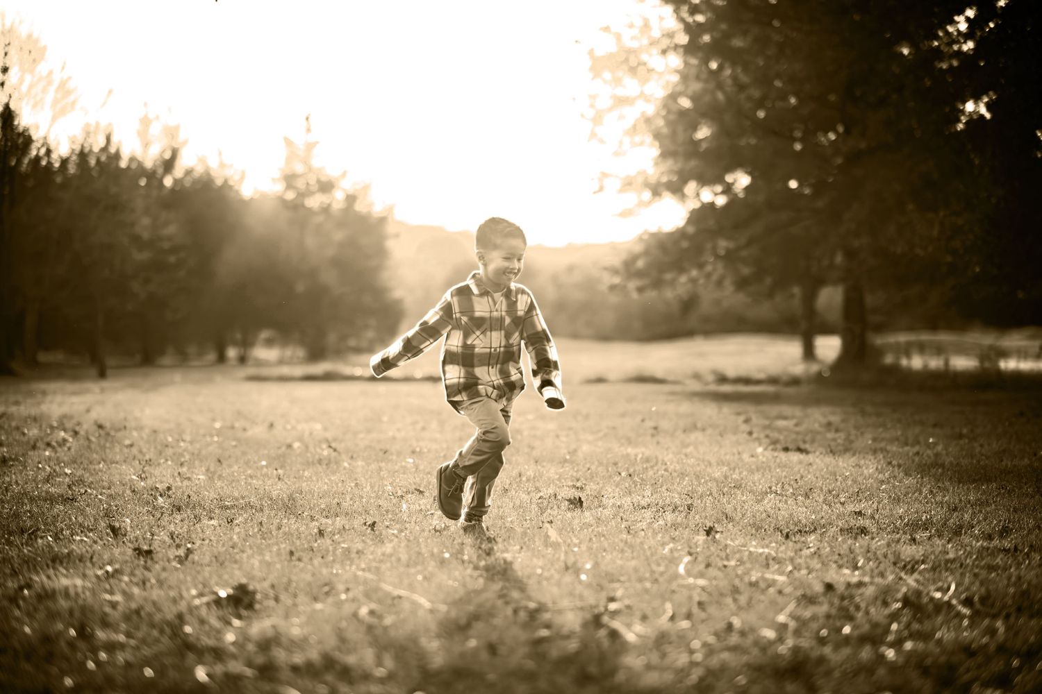 Young boy running through sunlit field during golden hour outdoor family photo session.