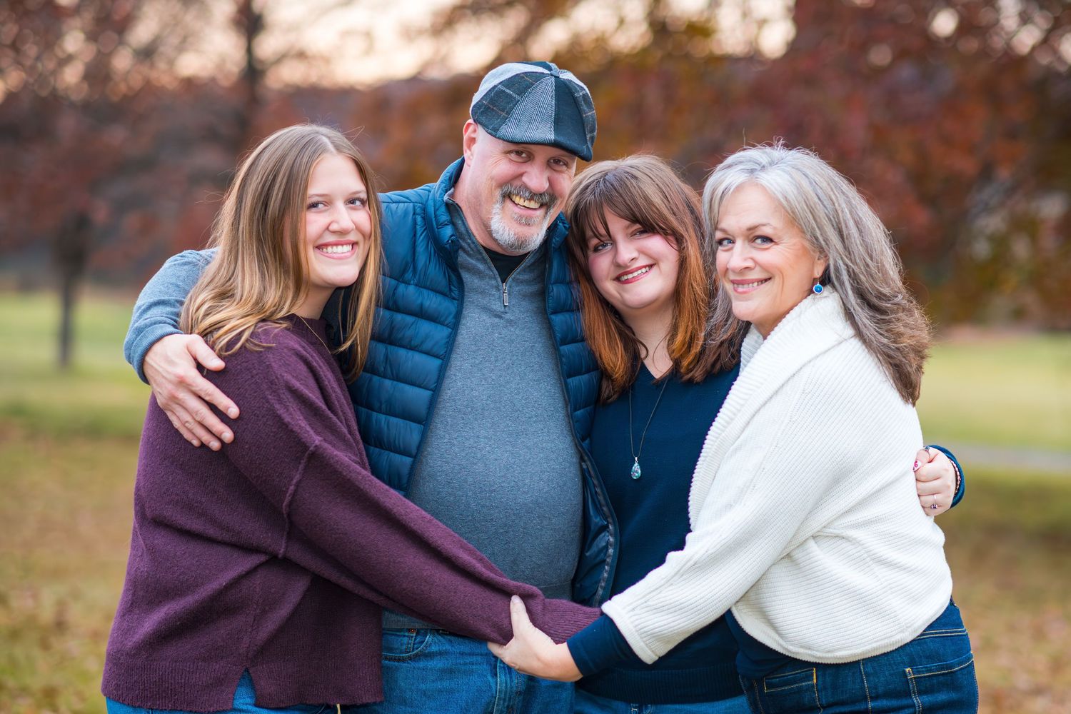 Happy family of four hugging and smiling together during autumn outdoor photo session.