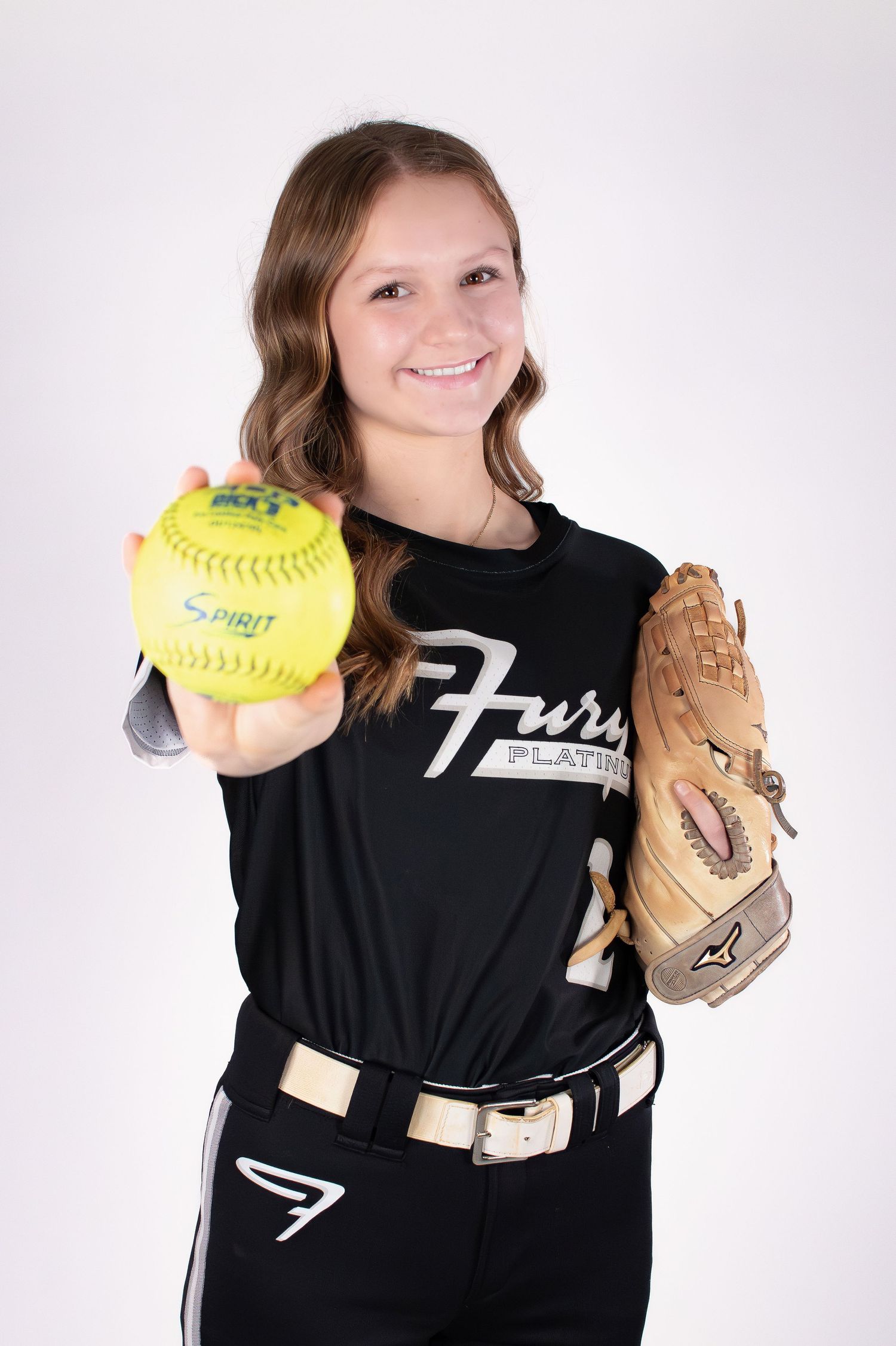 Smiling softball player in Fury Platinum jersey holding yellow Spirit softball and glove.