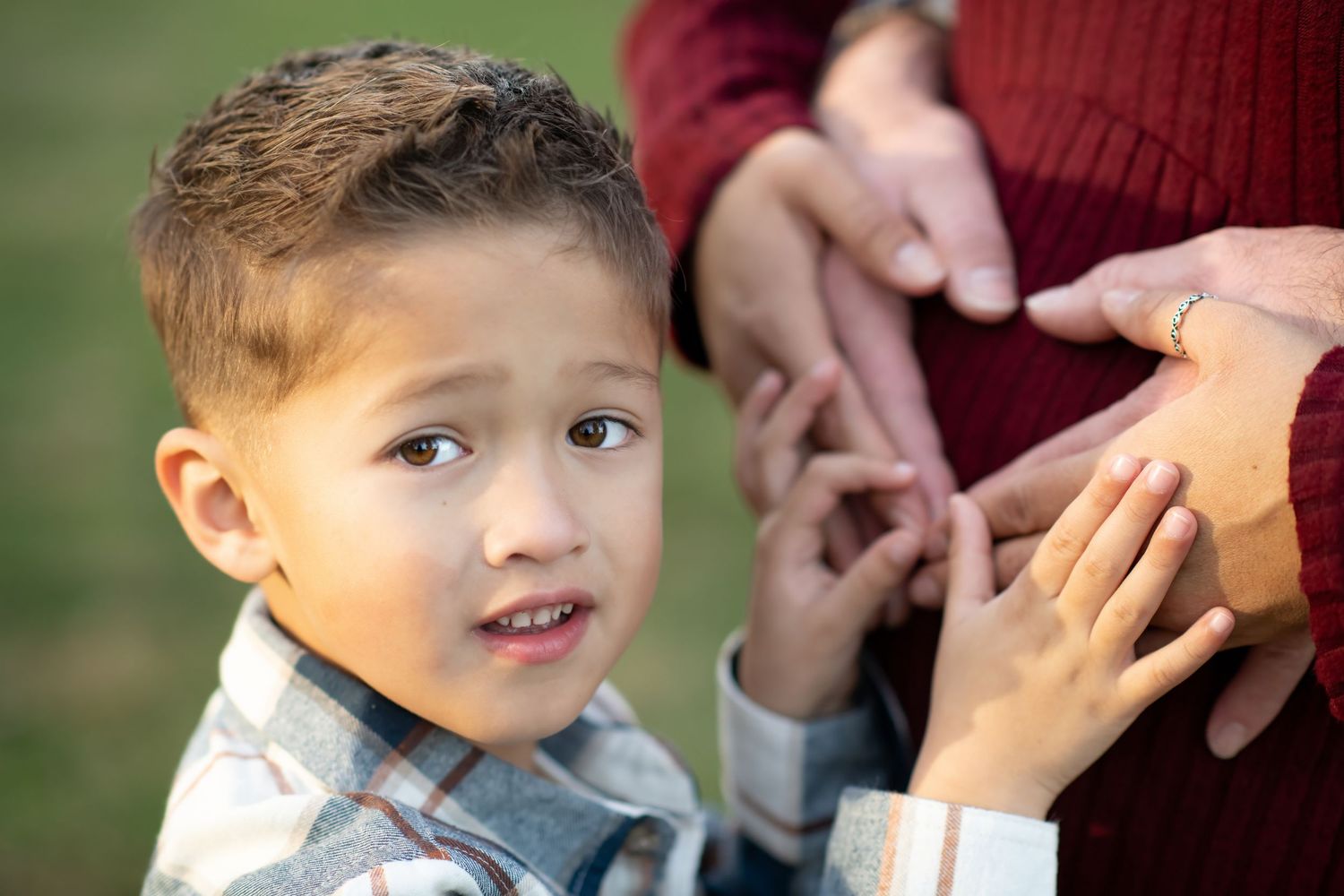 Young boy touching pregnant mother's belly outdoors during family maternity photo session.