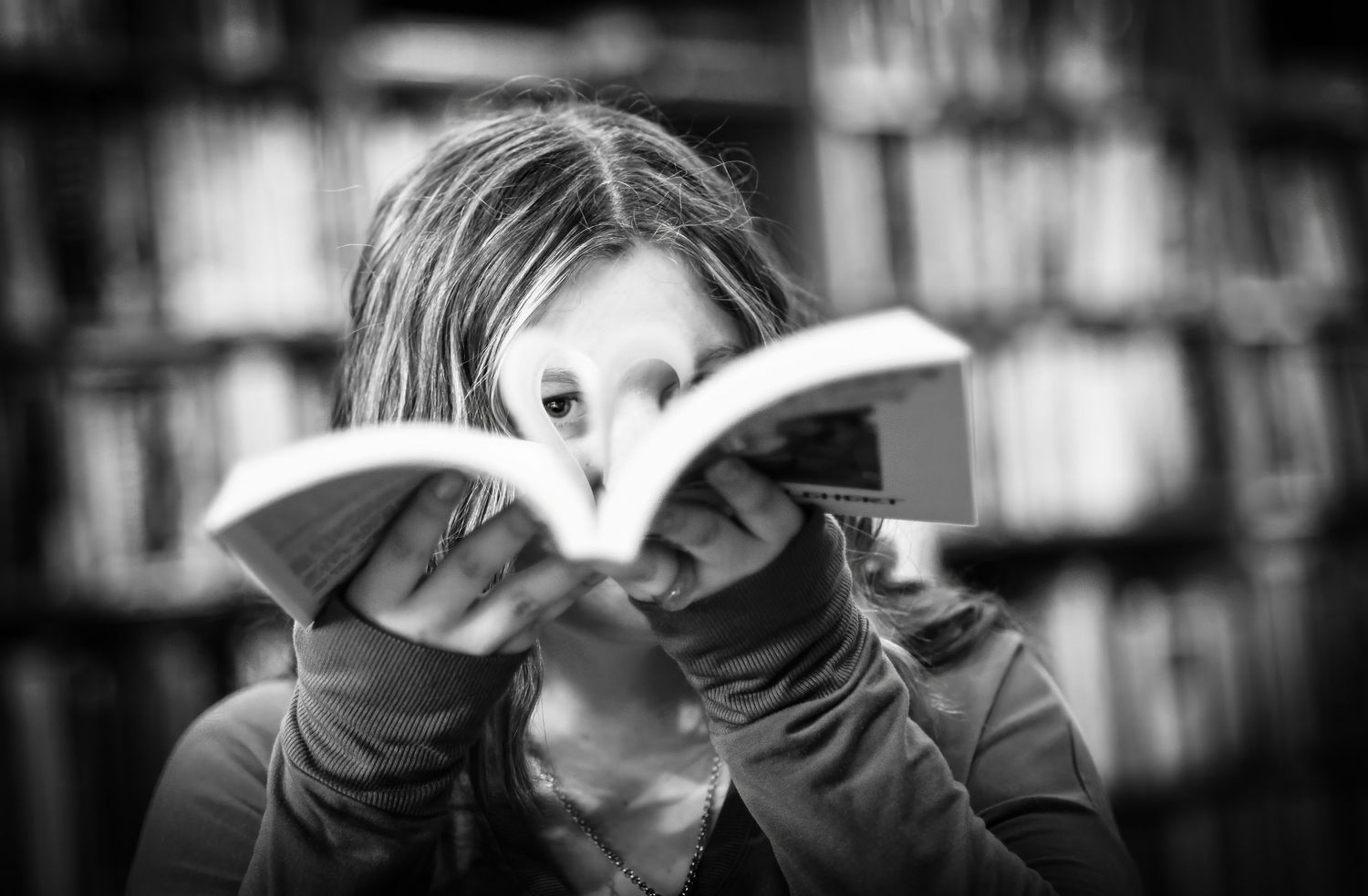 Child peeking over open book in black and white library photo.