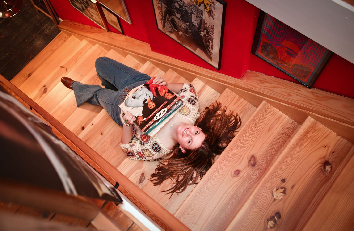 Overhead view of woman lying on wooden stairs holding colorful items.