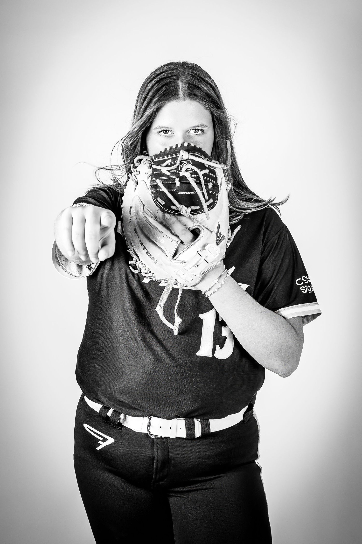 Black and white photo of softball player holding glove up to face in studio.