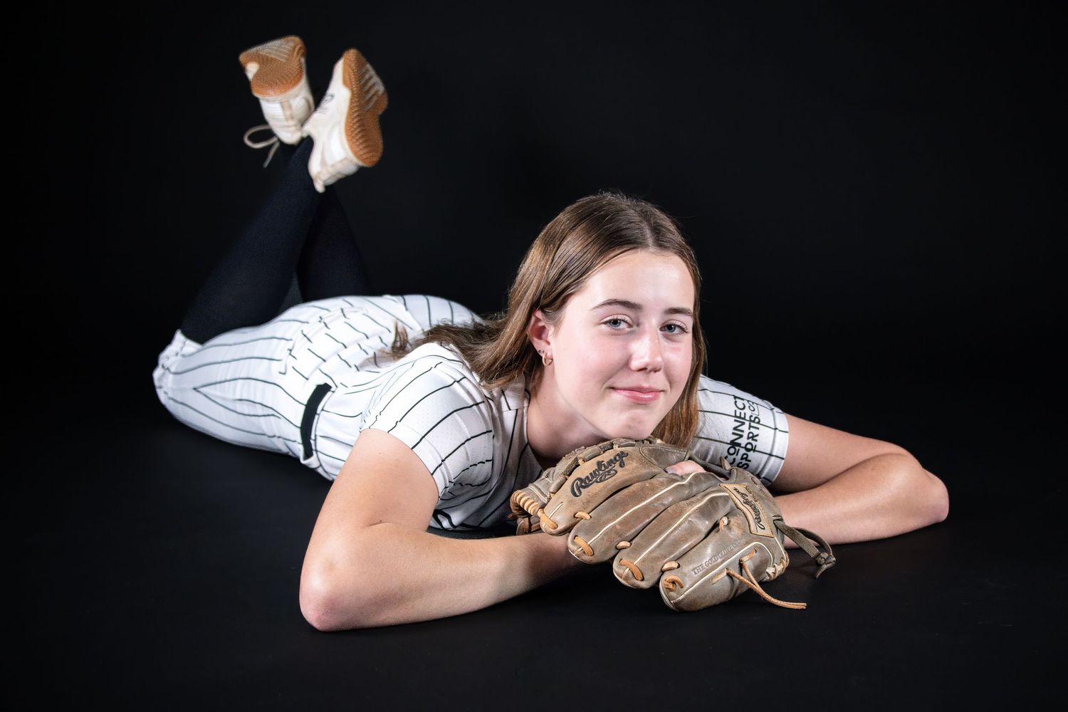 Softball player in pinstripe uniform lying on floor with glove smiling at camera in studio.