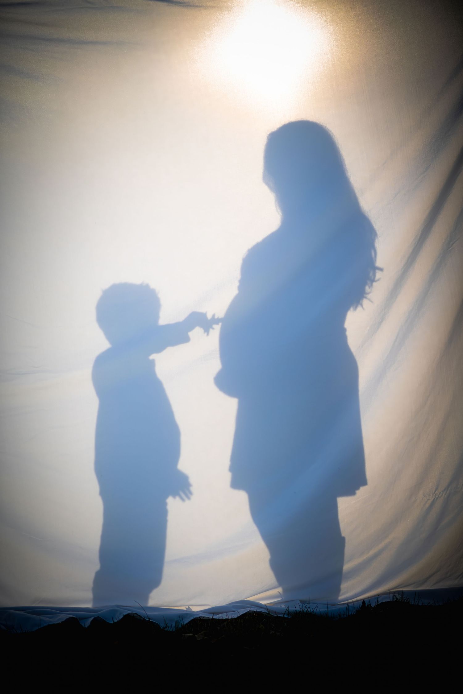 Silhouette of child and pregnant mother projected on white fabric backdrop.