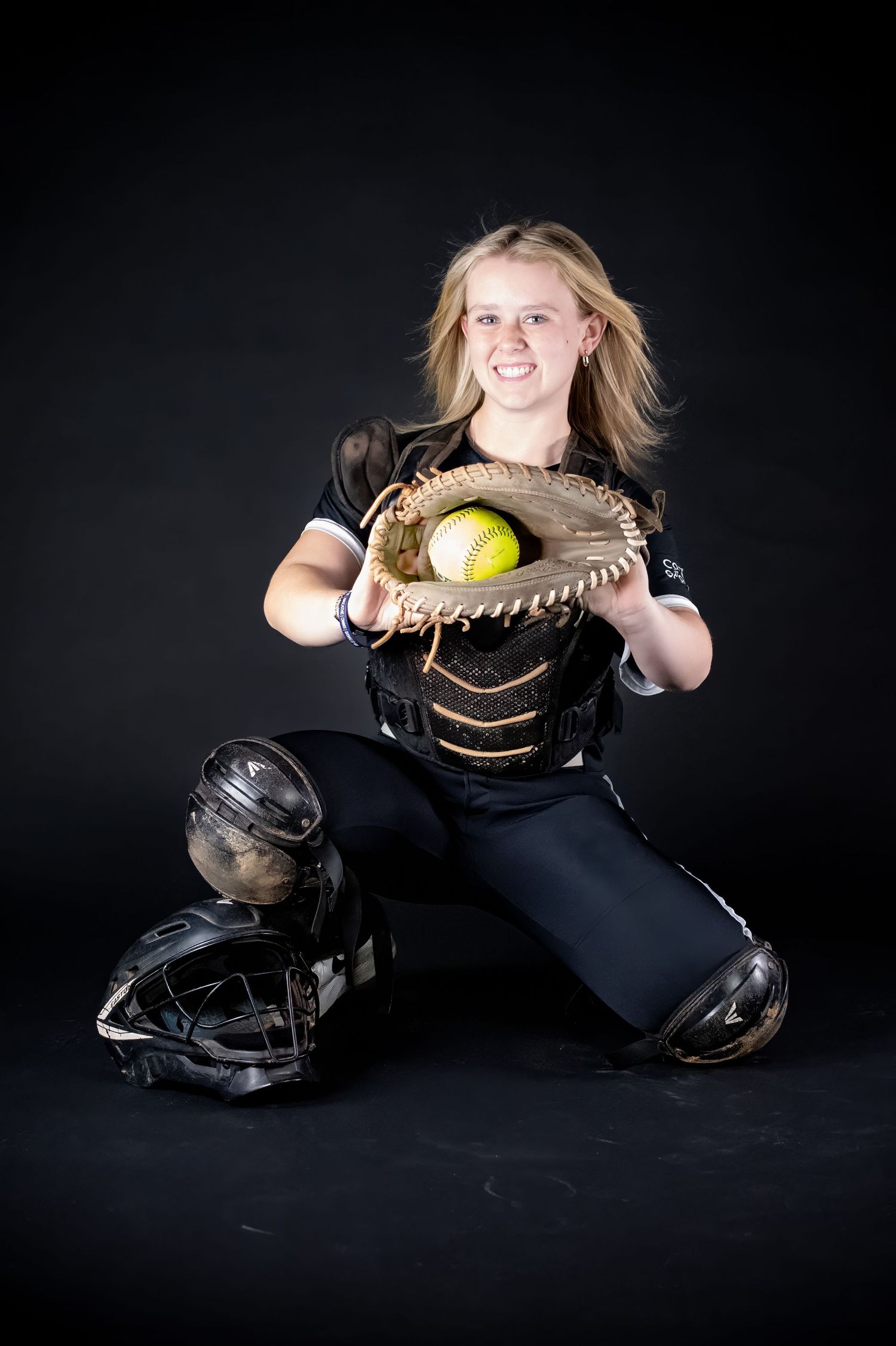 Female softball catcher in black uniform catching yellow softball in Easton catcher gear.