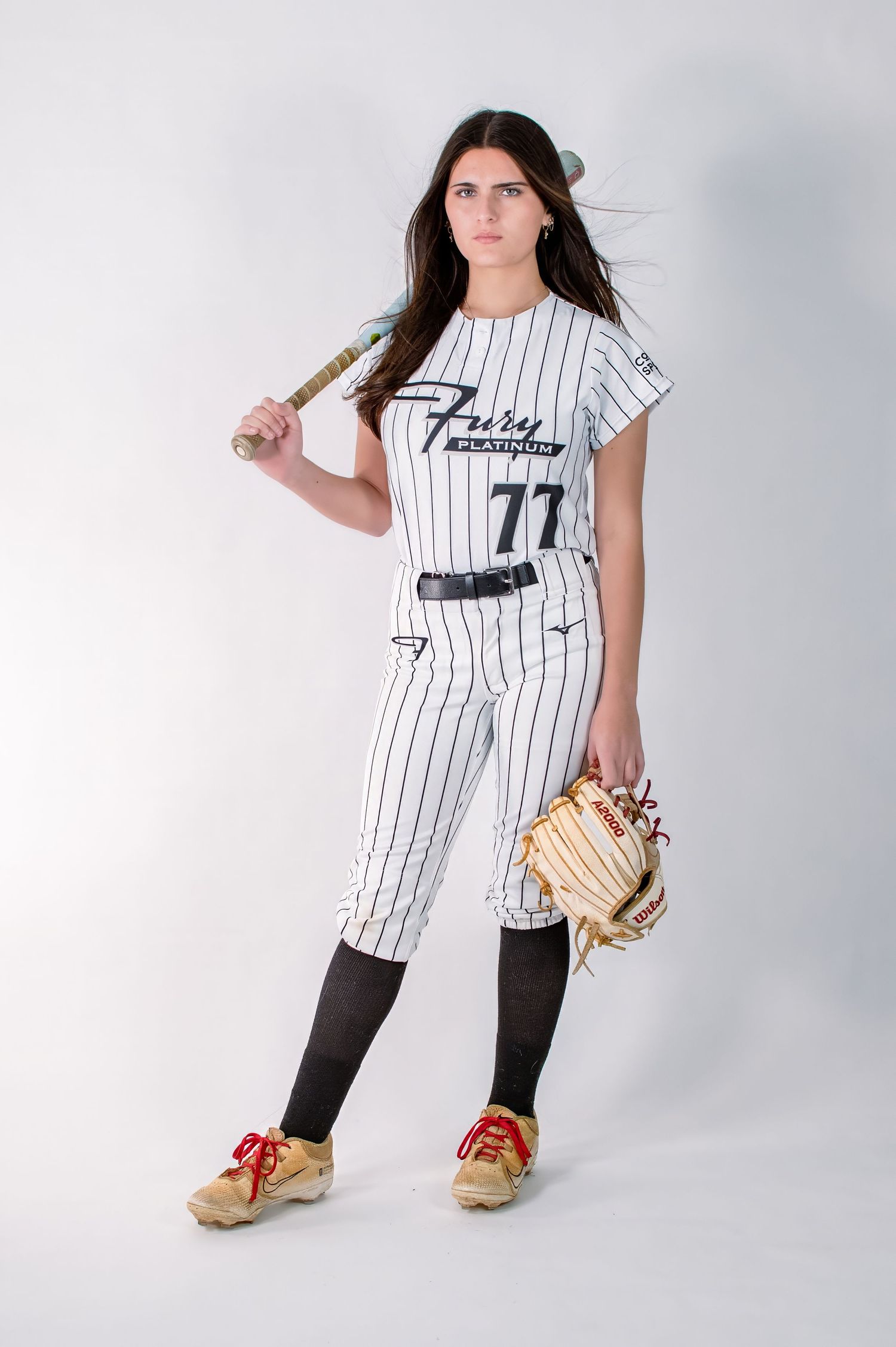 Female softball player #77 in Fury Platinum pinstripe uniform holding bat and glove.